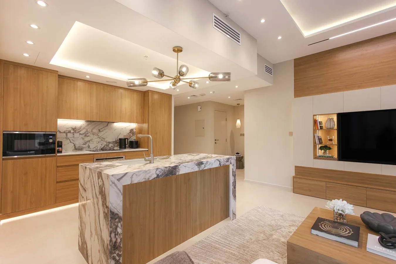 Una cocina moderna abierta al salón, con una isla de mármol y armarios de madera.