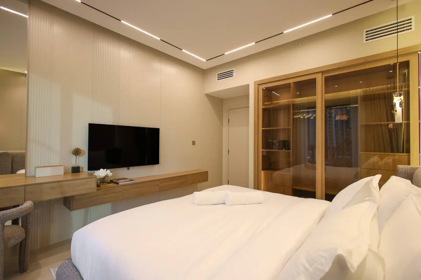 Un dormitorio luminoso con una cama bien tendida, televisor y armarios de madera empotrados.