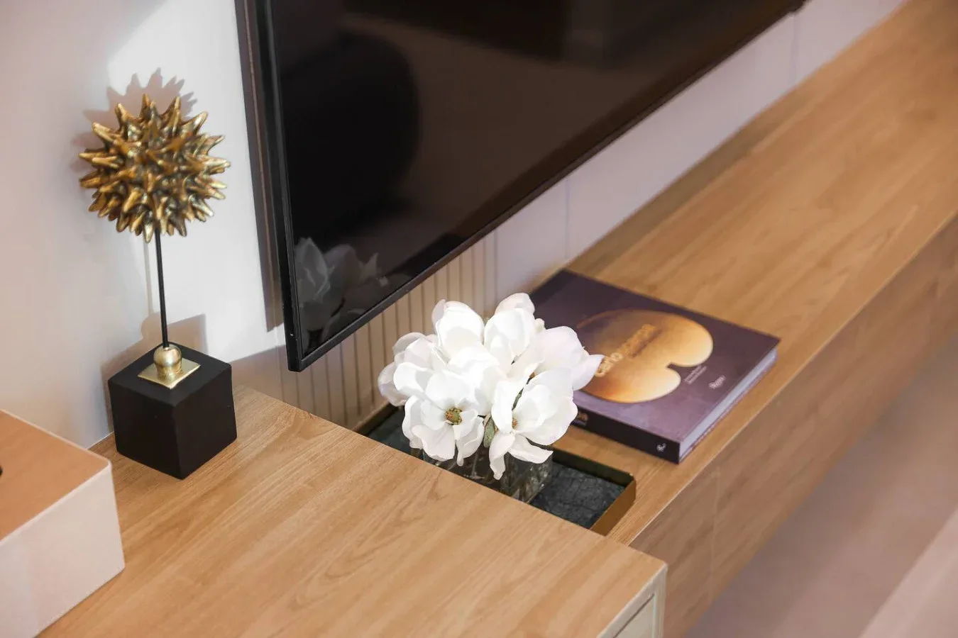 Un televisor está sobre un mueble de madera decorado con flores blancas.