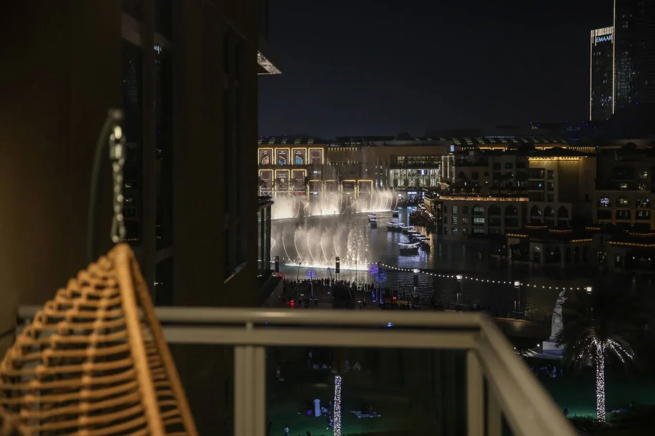 Vista nocturna de fuentes y edificios iluminados desde un balcón.