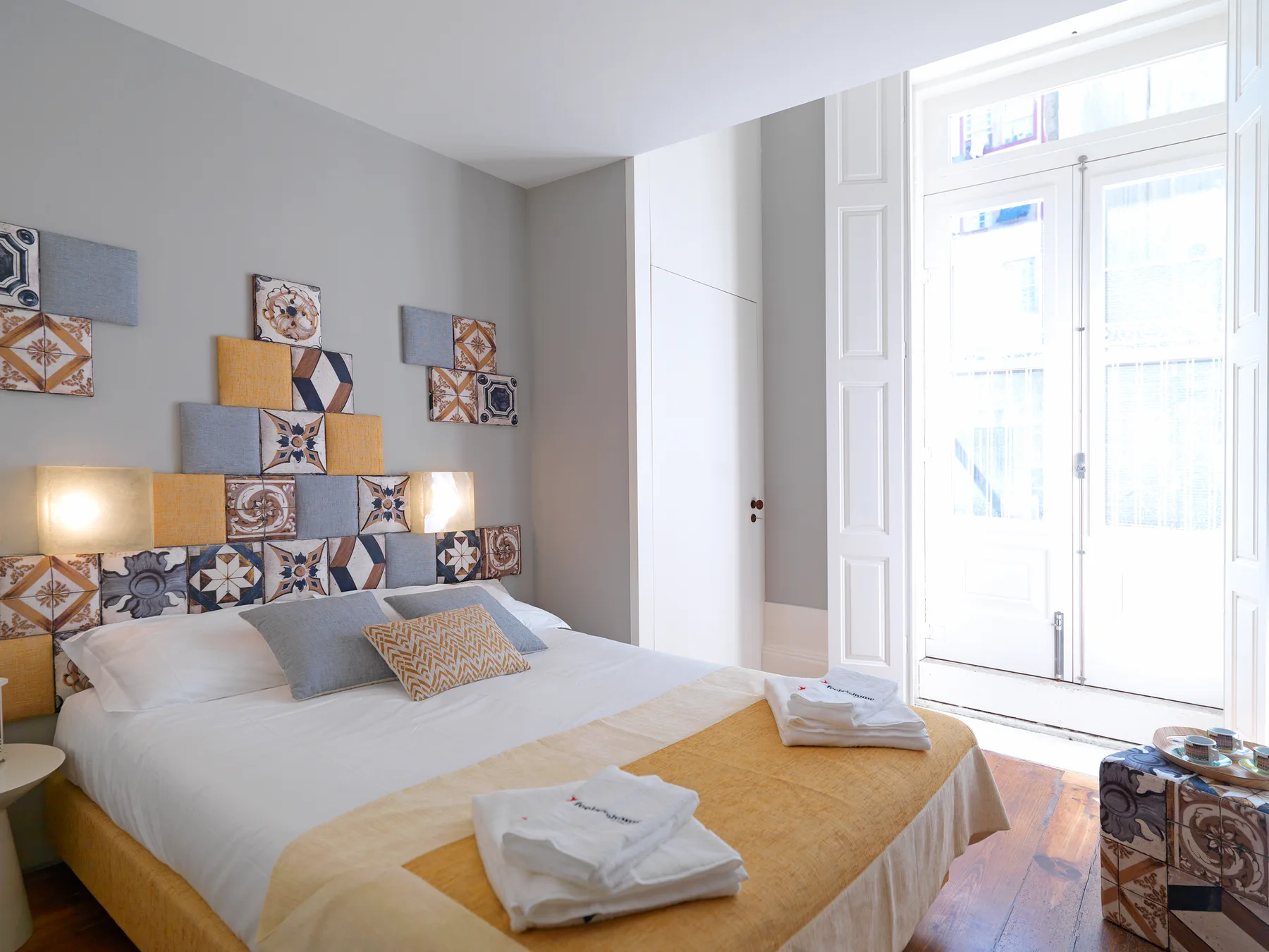 A bright bedroom with a bed beneath decorative patterned tiles.