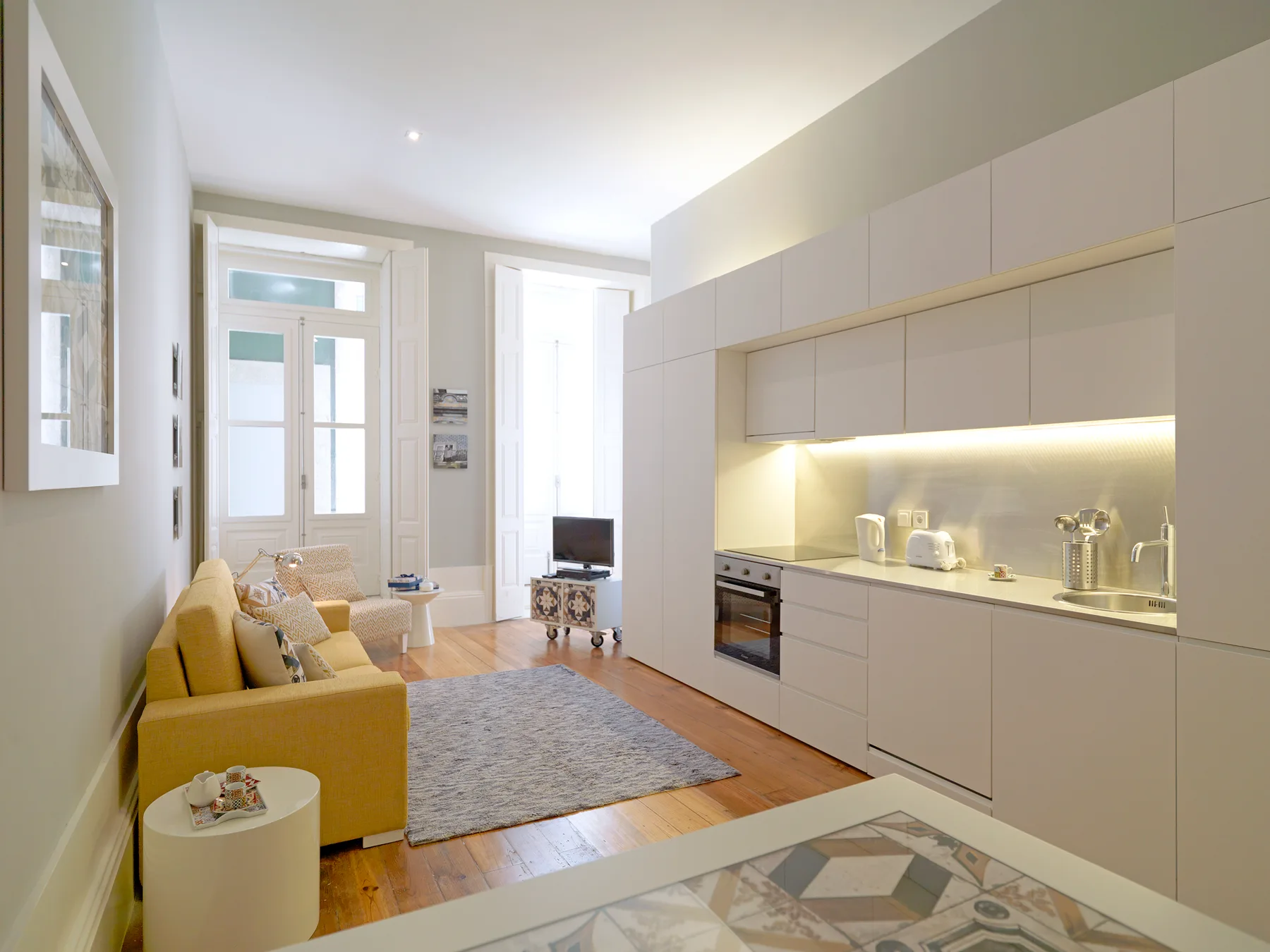 A bright living room with a yellow seating area beside a modern kitchen.
