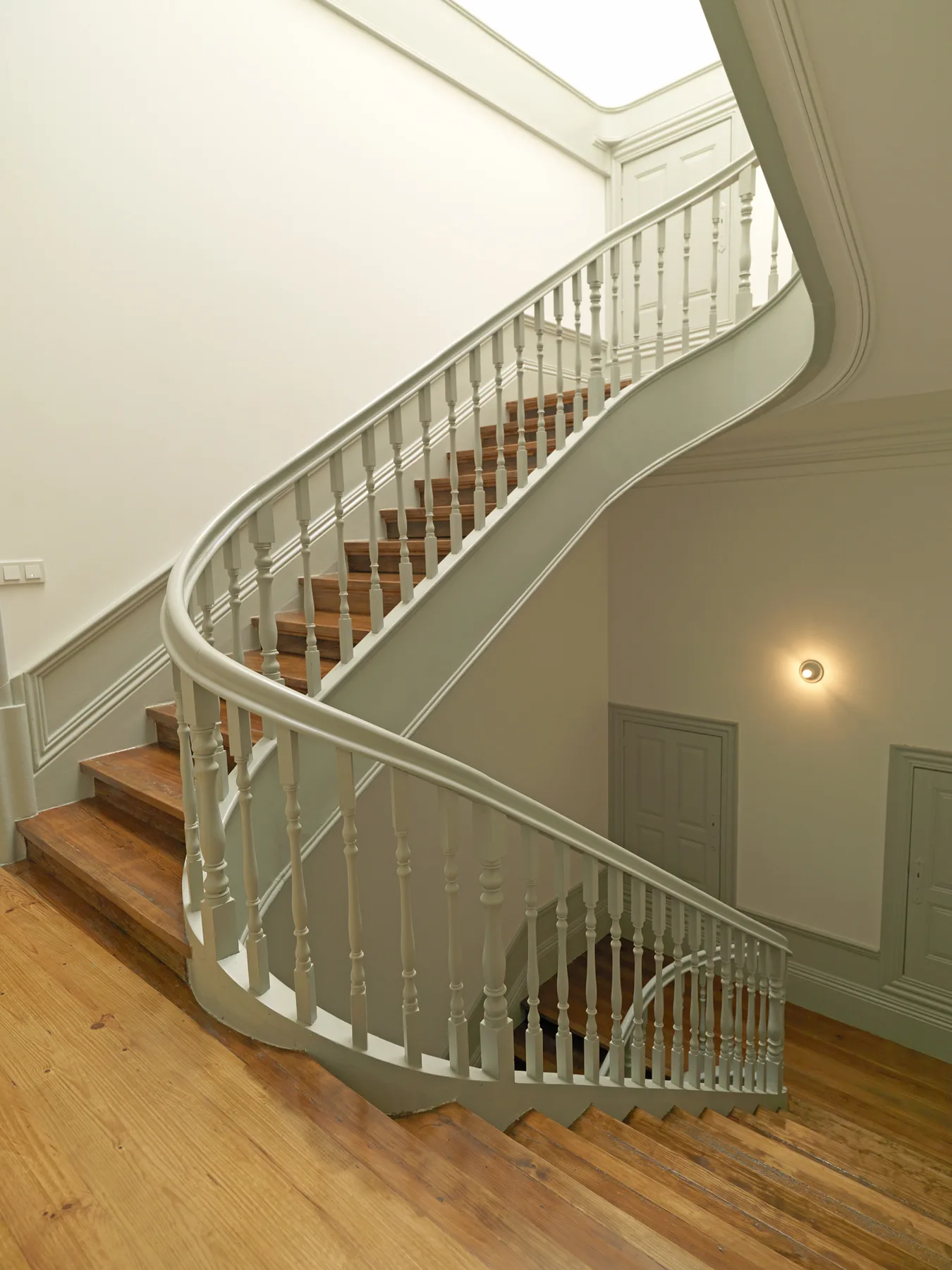 A curved wooden staircase with pale railings rises through a bright interior.