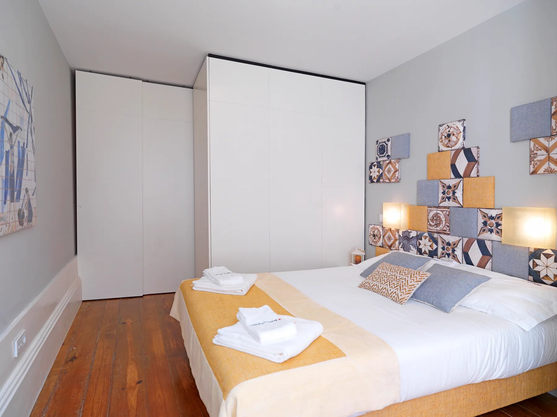 A bedroom with a neatly made bed and colorful patterned wall tiles.