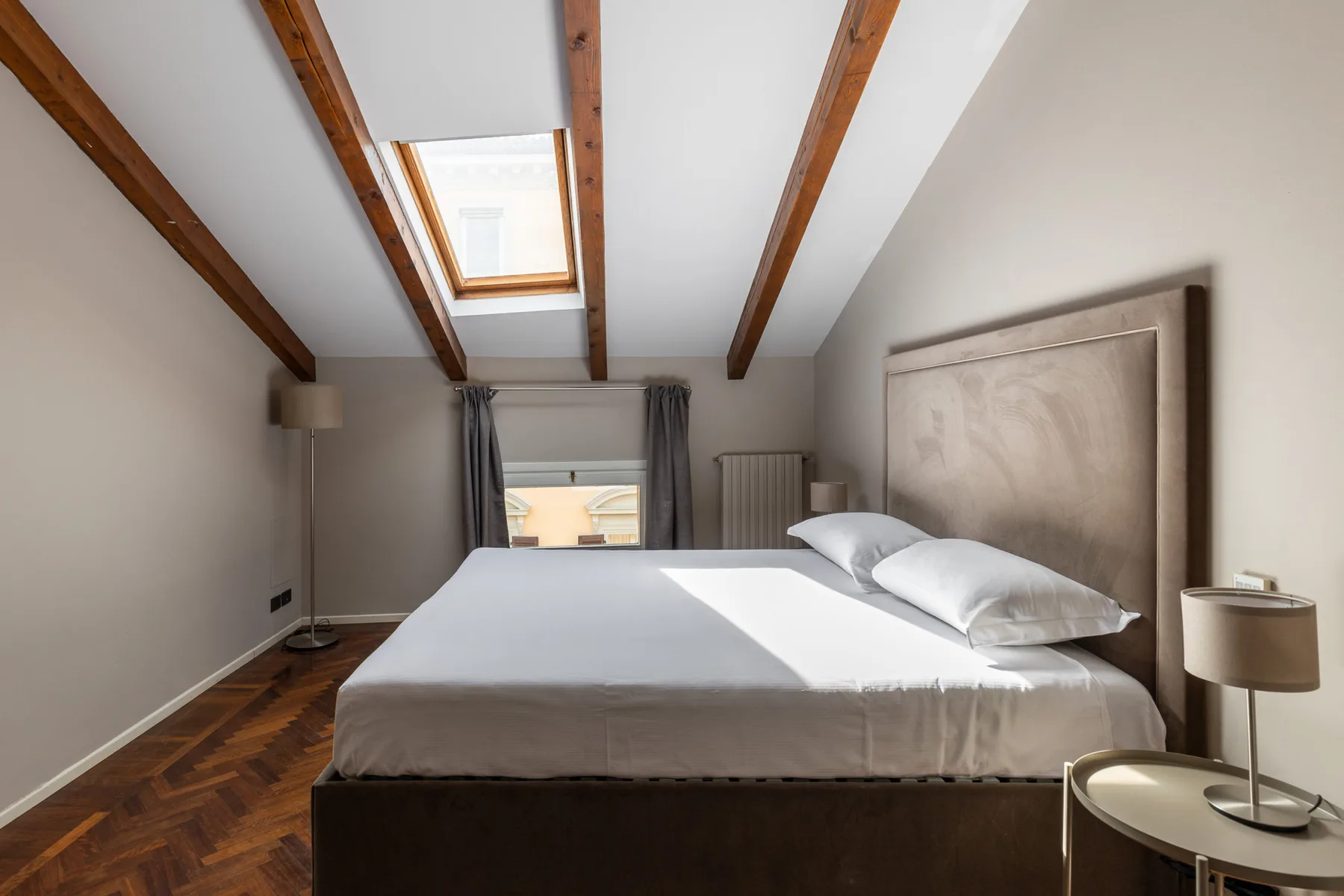 Un dormitorio con una cama grande bajo vigas de techo expuestas y una claraboya.