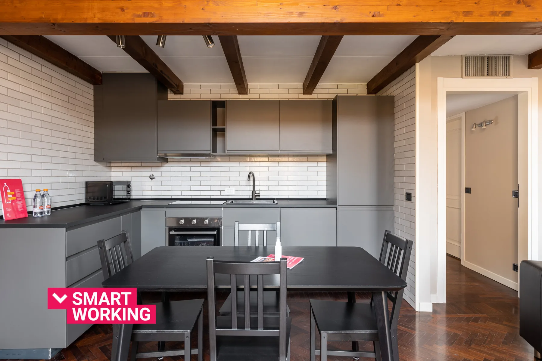 Una cocina moderna con gabinetes grises, una mesa de comedor y vigas expuestas en el techo.