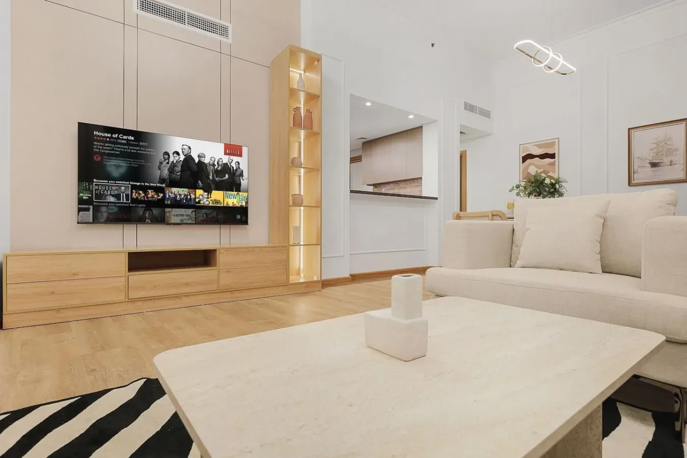 Una sala luminosa con un televisor en la pared y una zona de asientos de tonos claros.