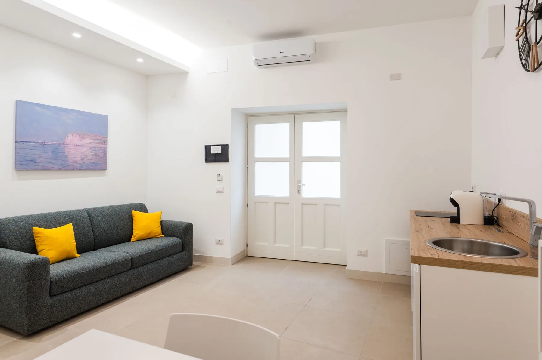 A bright living area with a dark sofa and a small kitchen counter.