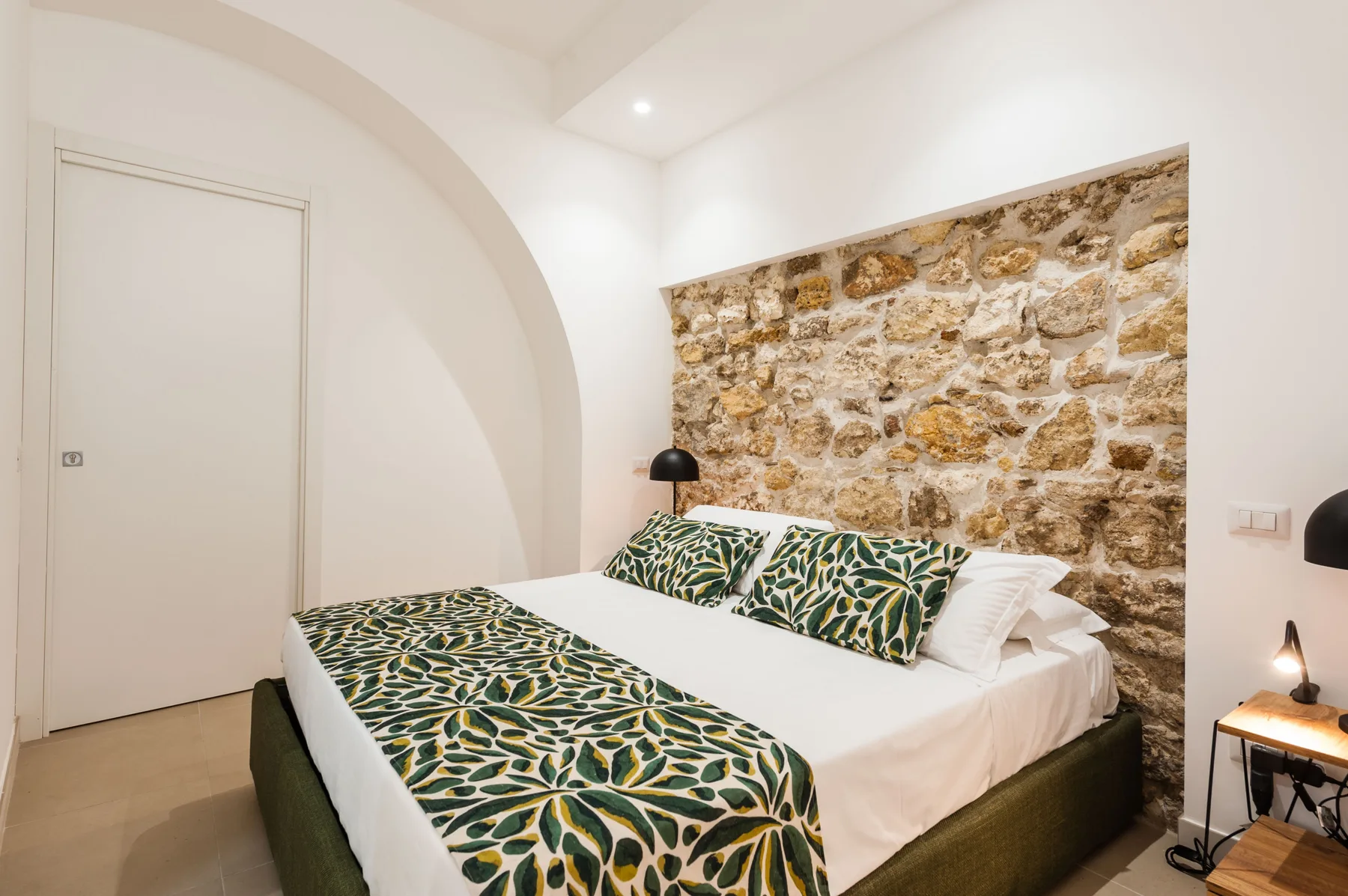 A bedroom with a double bed dressed in green and yellow patterned bedding.