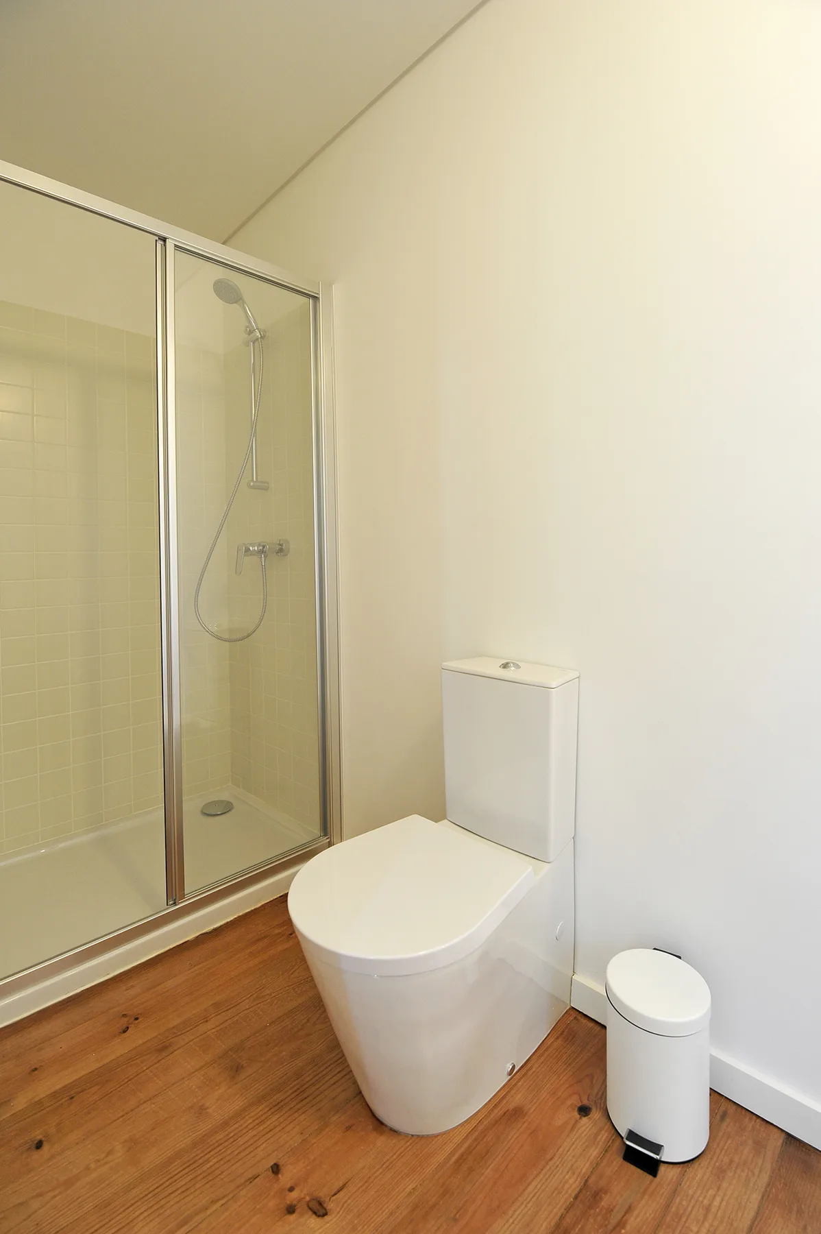 Un baño con una ducha de cristal, un inodoro y suelo de madera.