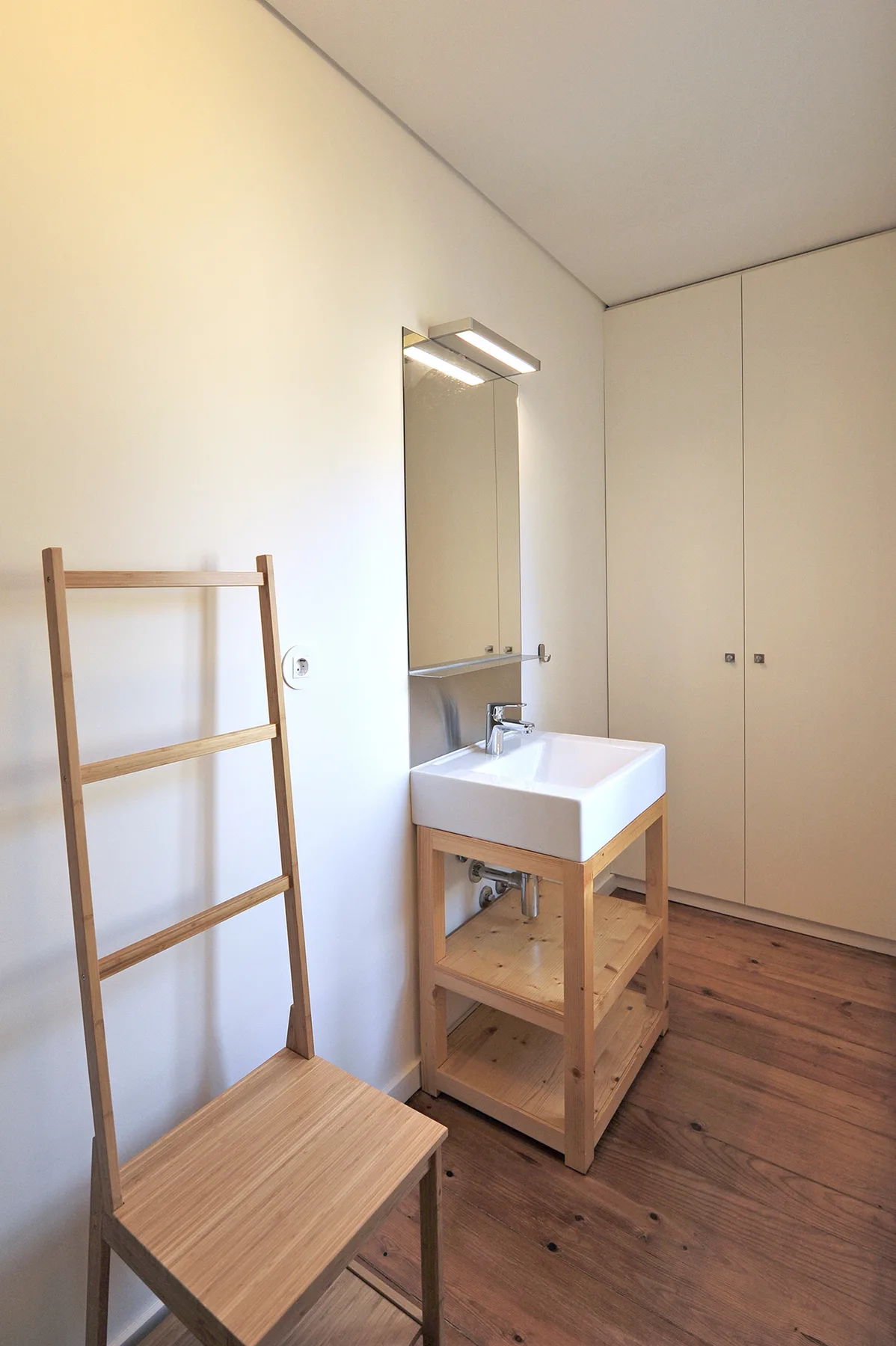 Un lavabo de baño con espejo y una silla de madera al lado.