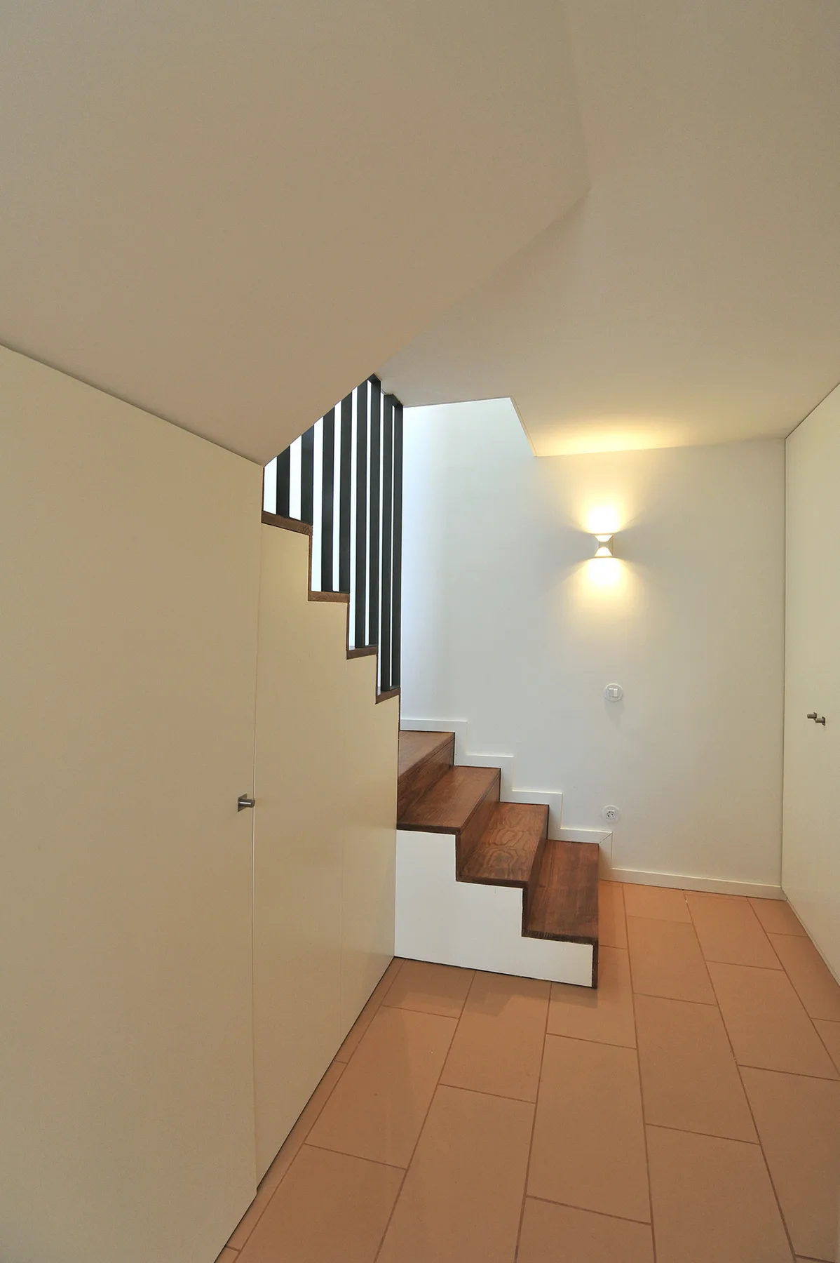 Un pasillo interior con una escalera y una lámpara de pared.