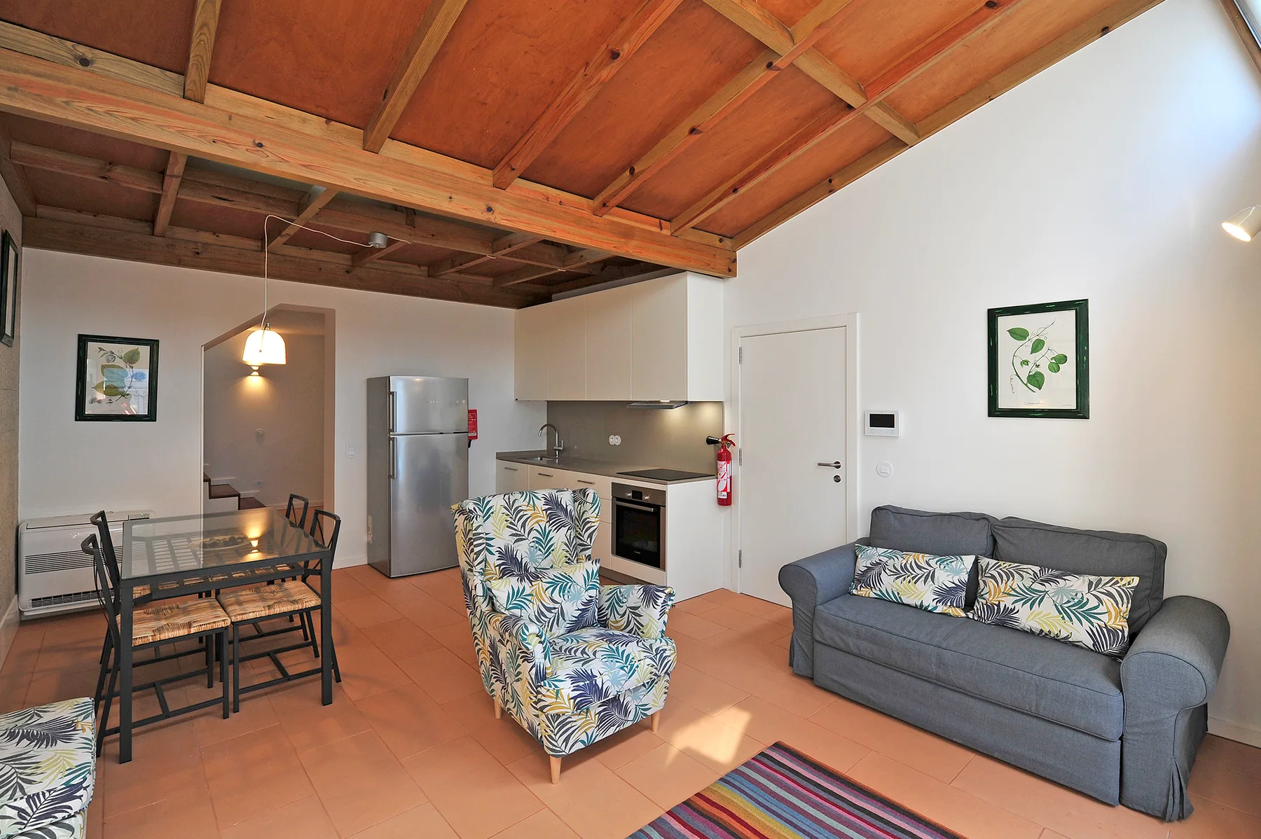 Sala de estar y cocina con mesa de comedor, asientos y vigas de madera a la vista.