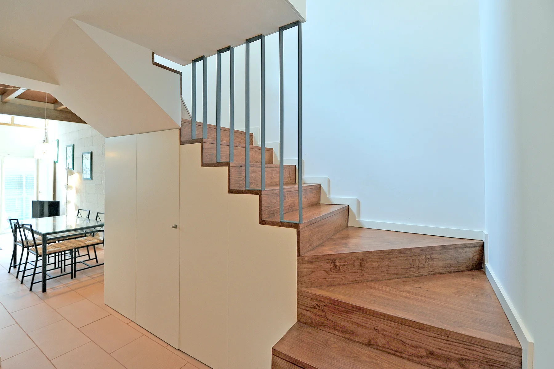 Una escalera interior moderna con peldaños de madera y barandillas verticales delgadas.