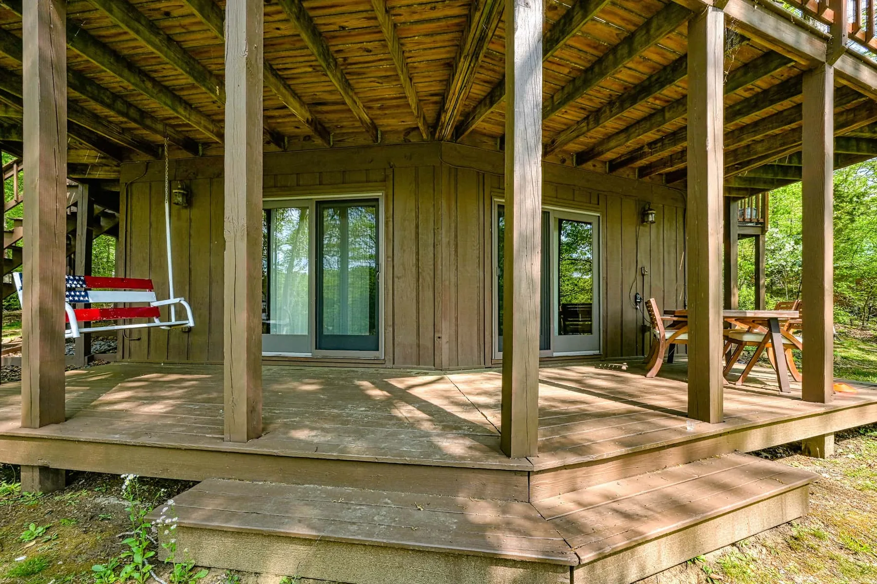 A covered wooden deck with glass doors and outdoor seating.