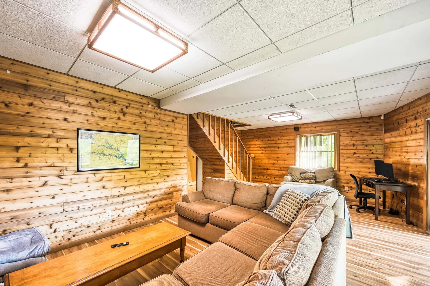 Sala con paredes de madera, asientos seccionales y un escritorio junto a la ventana.