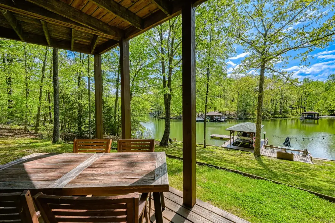 Una terraza de madera con una mesa da a un lago rodeado de árboles.