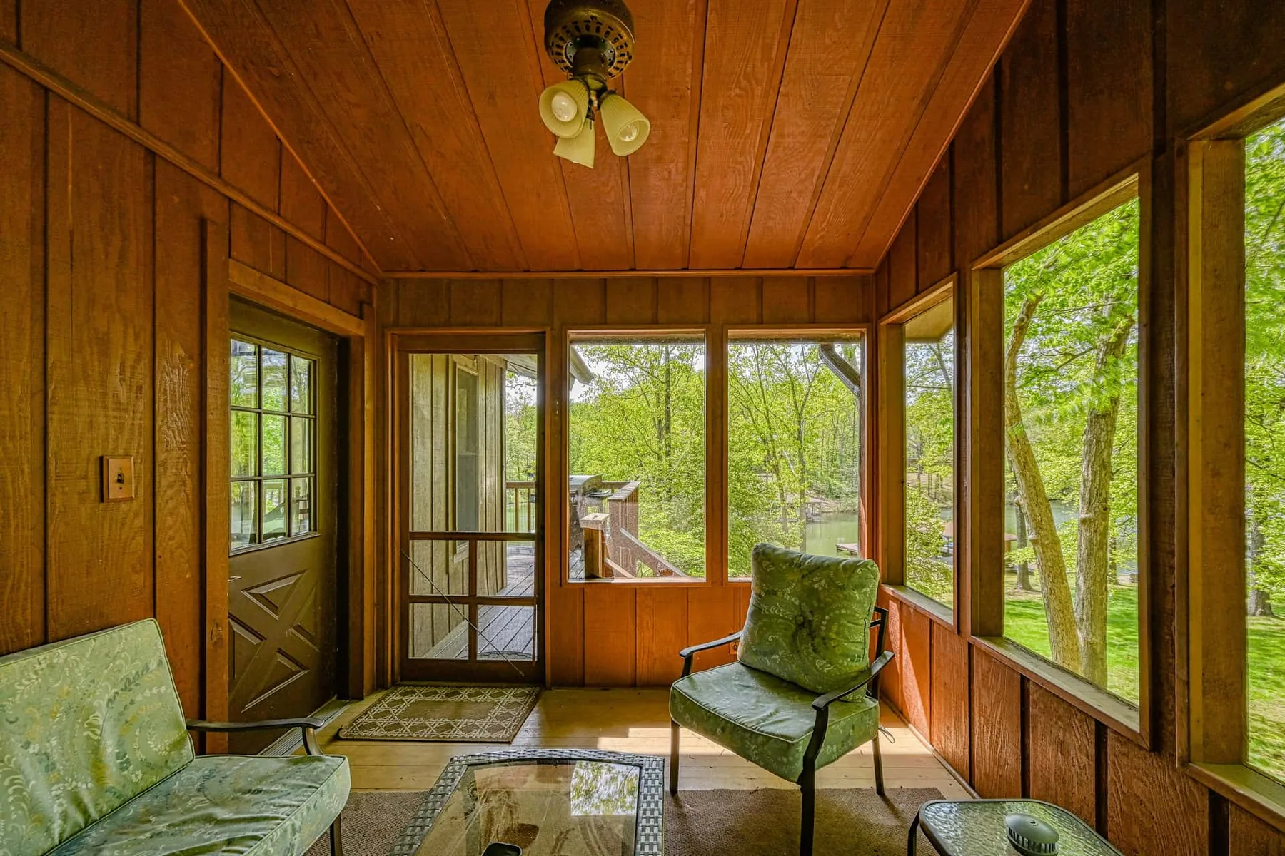 Un solárium revestido de madera con grandes ventanas y asientos verdes.