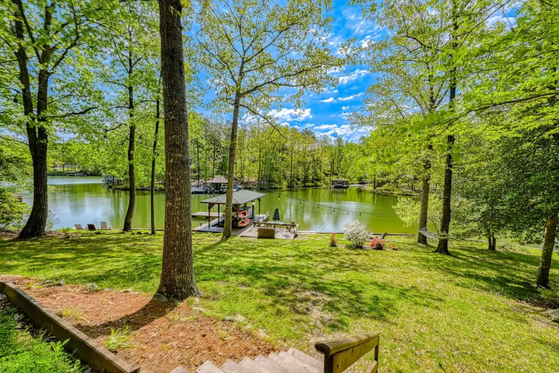Una zona junto al lago con césped, árboles frondosos y un pequeño muelle.