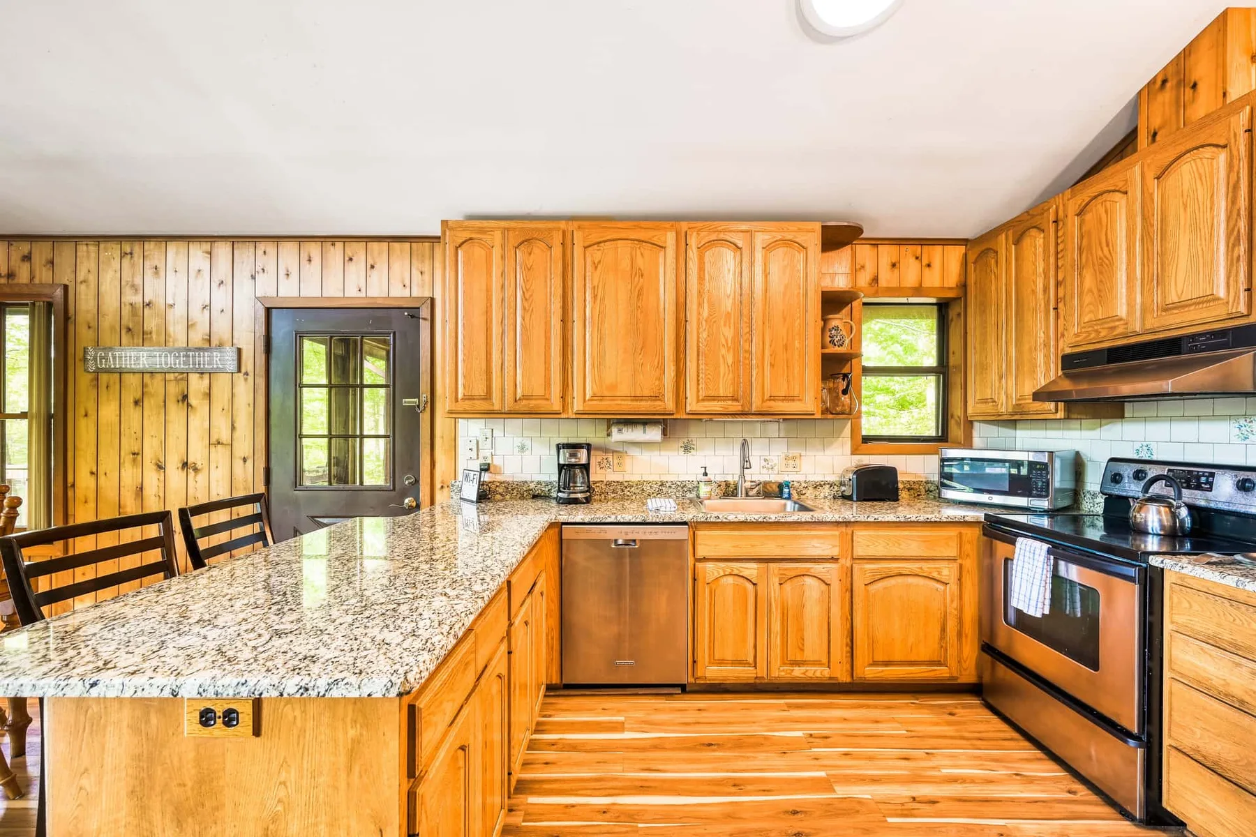 Cocina con paredes de madera, gabinetes de madera, una isla central y electrodomésticos de acero inoxidable.