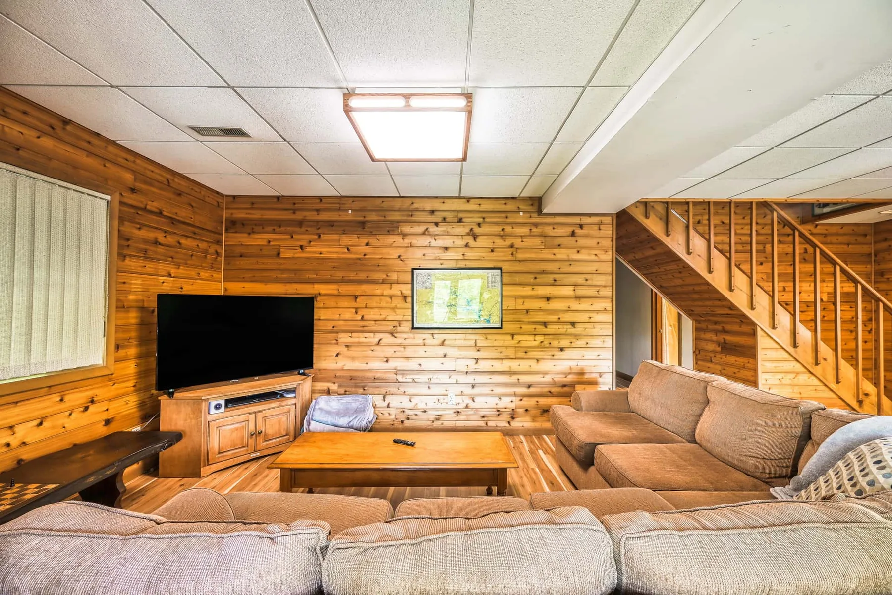 Sala de estar revestida de madera con asientos, un televisor y una escalera.