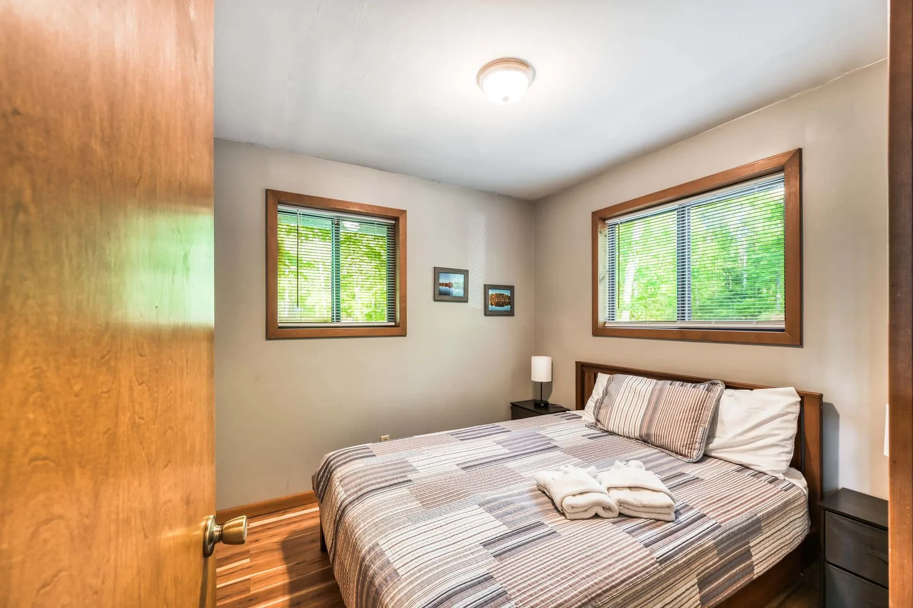 Un dormitorio con una cama ordenada y dos ventanas con persianas.