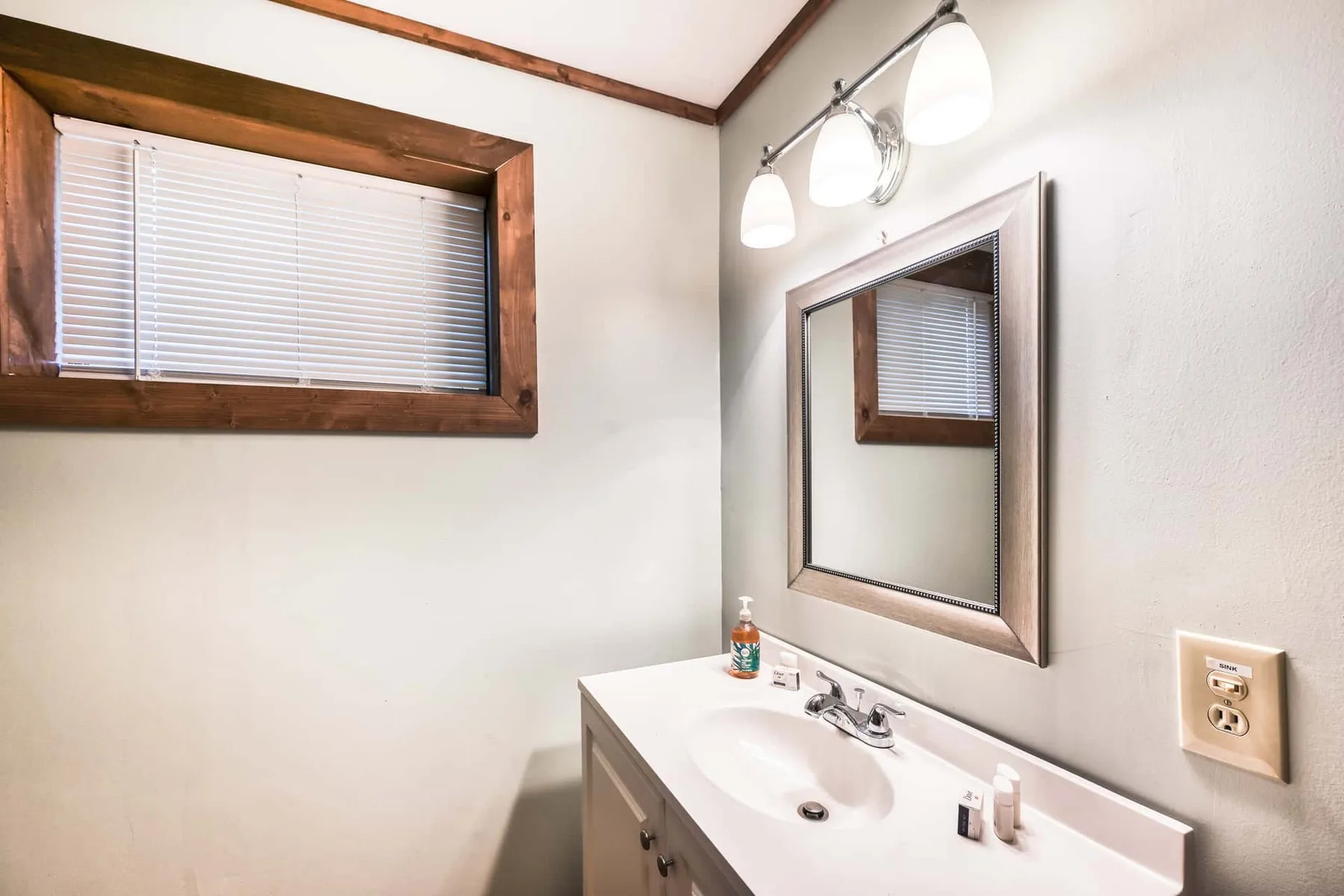 Un lavabo de baño con espejo y luz sobre la pared.