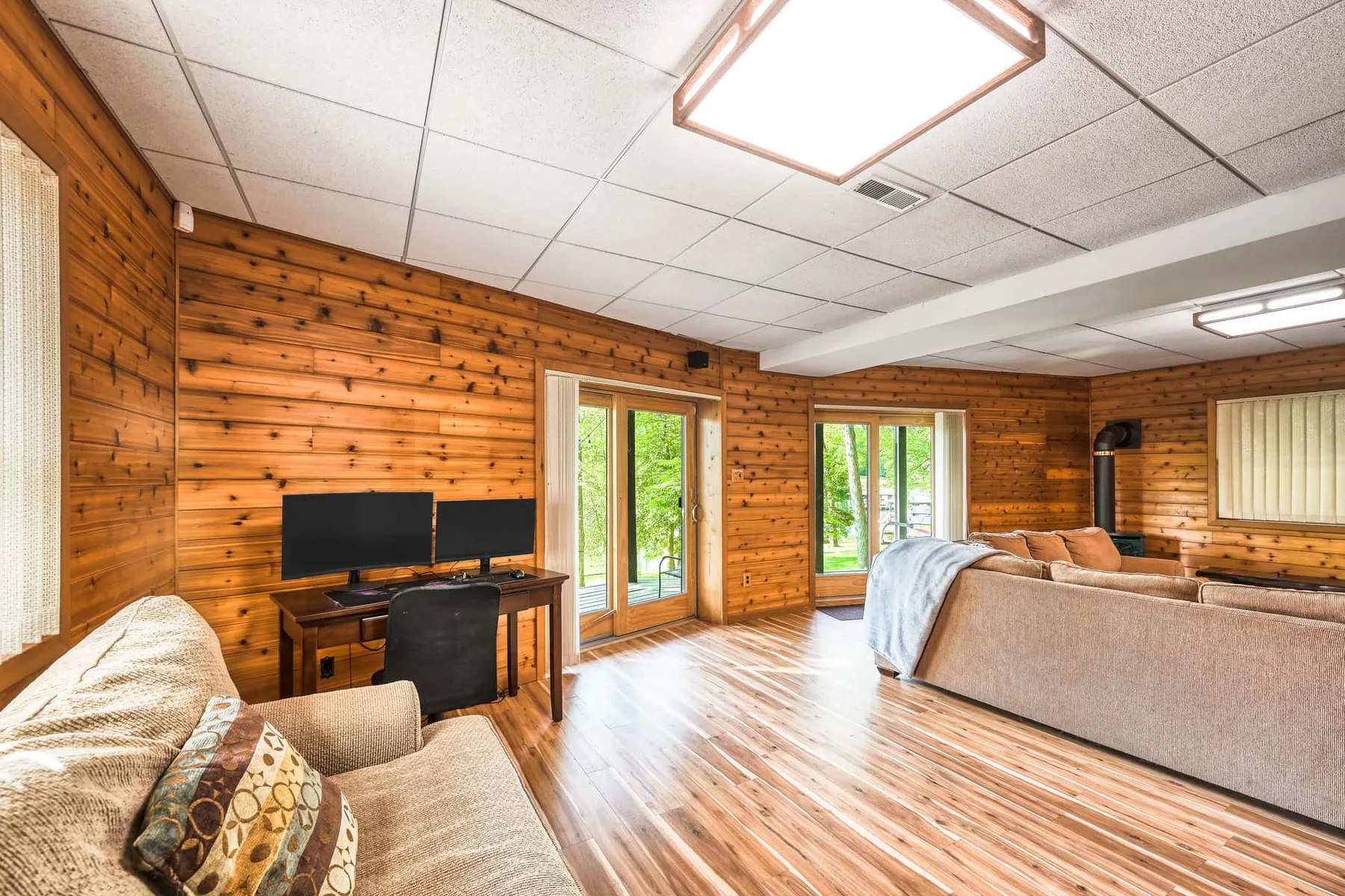 Una sala con paredes de madera, asientos, un televisor y puertas de vidrio al exterior.