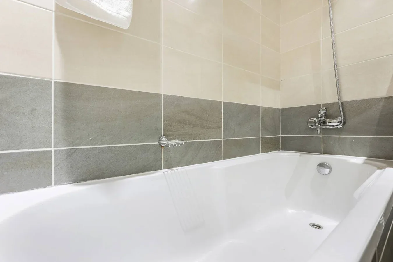 Un baño alicatado con una bañera blanca y una ducha montada en la pared.