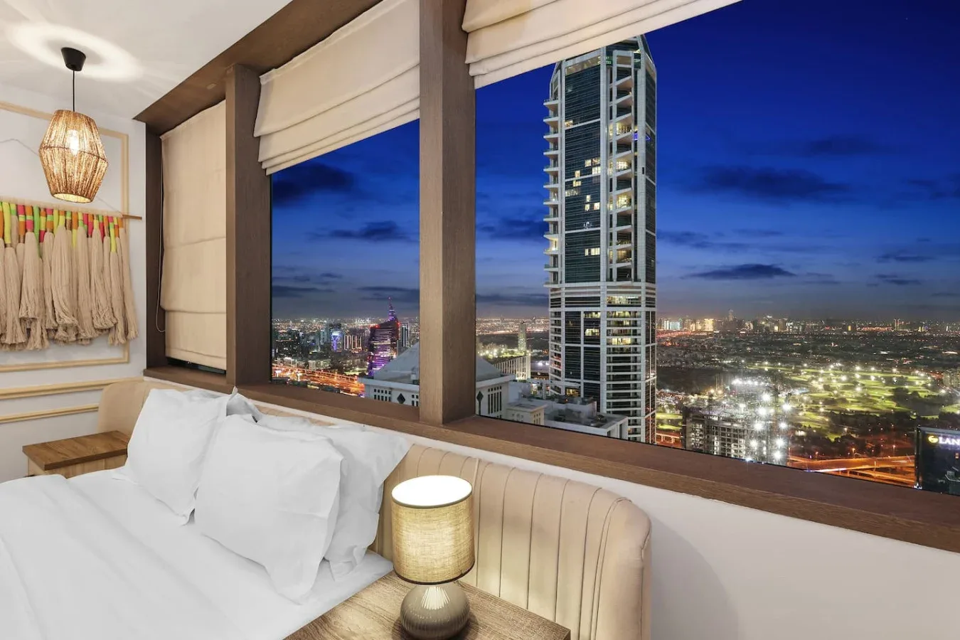 Un dormitorio con una cama junto a grandes ventanas con vistas a la ciudad de noche.