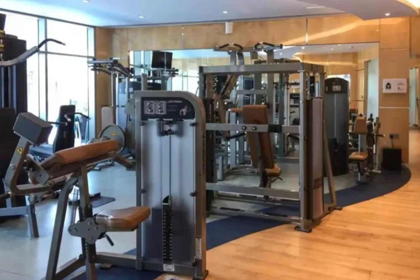 Un gimnasio con máquinas de ejercicio alrededor de una zona de entrenamiento con espejos.