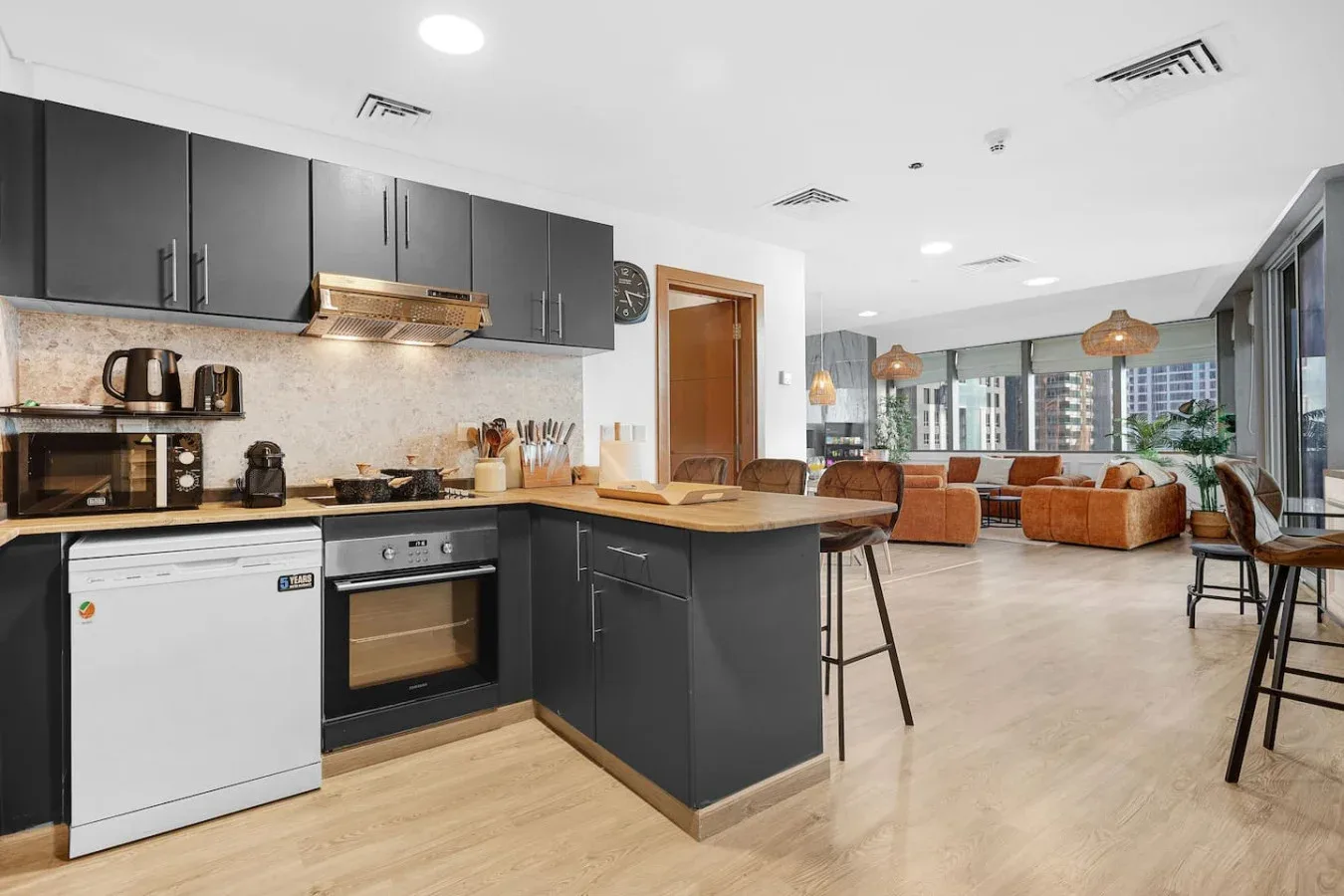 Cocina y sala de estar de concepto abierto, con gabinetes oscuros y asientos junto a grandes ventanas.