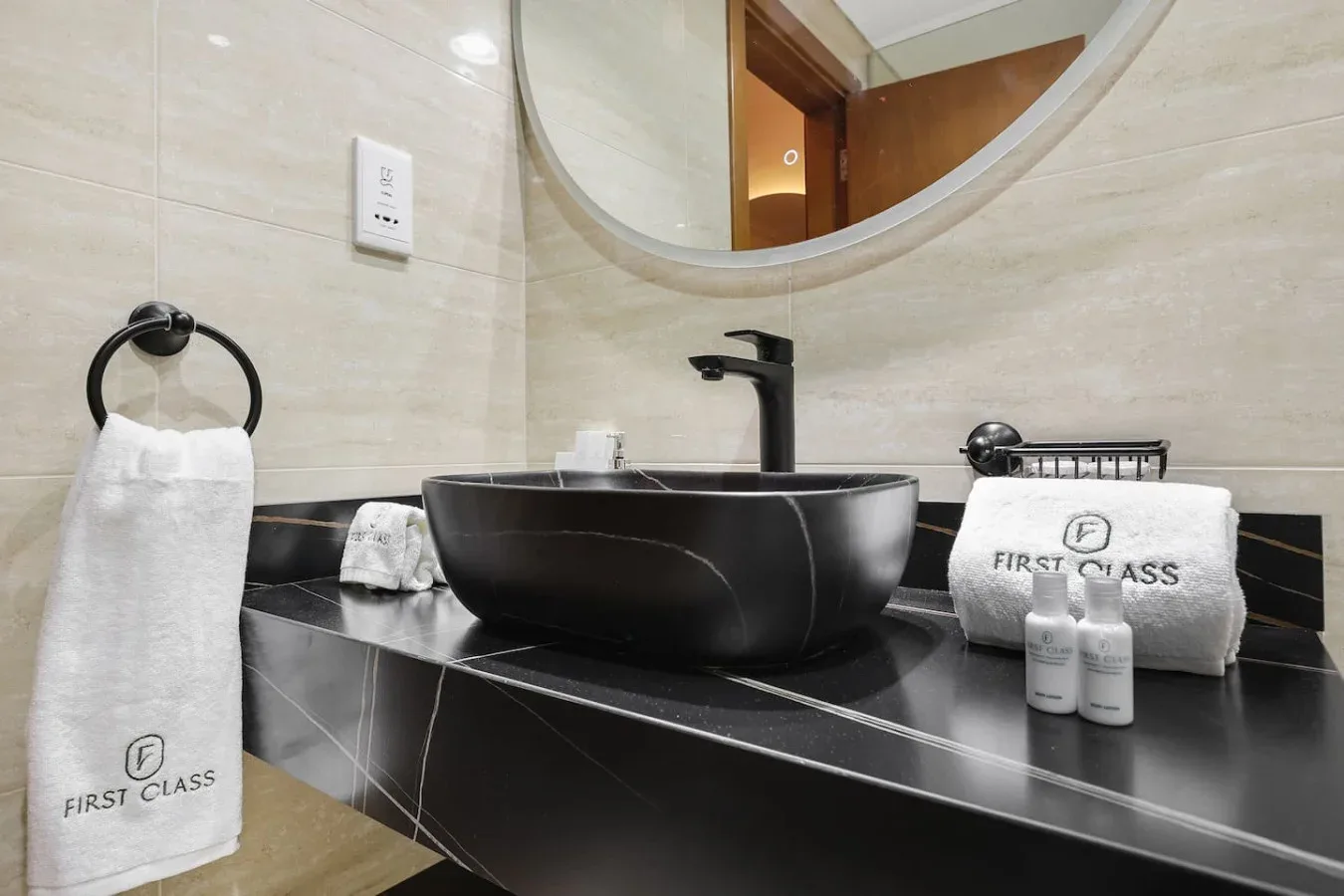 Un lavabo de baño tiene un lavamanos oscuro bajo un espejo redondo.