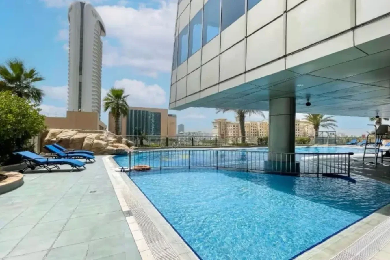 Una piscina al aire libre junto a un edificio moderno, con asientos en la terraza.