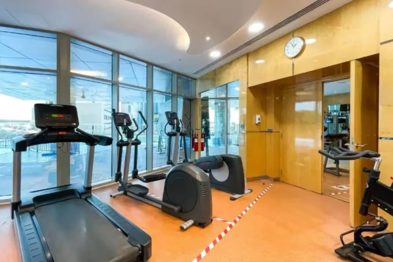 Un gimnasio con máquinas de ejercicio junto a grandes ventanas.