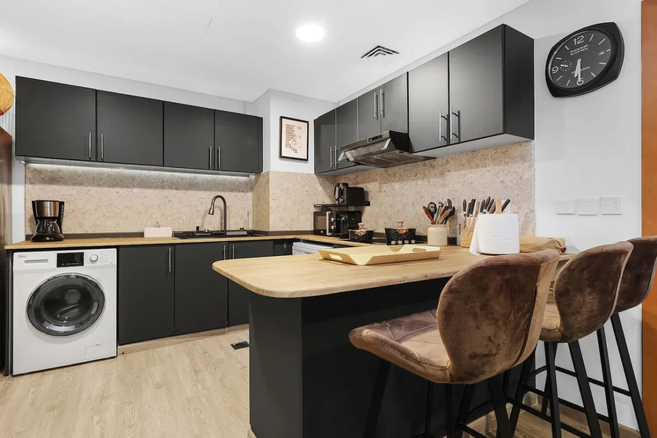Una cocina moderna con gabinetes oscuros, una lavadora y una barra para desayunar.