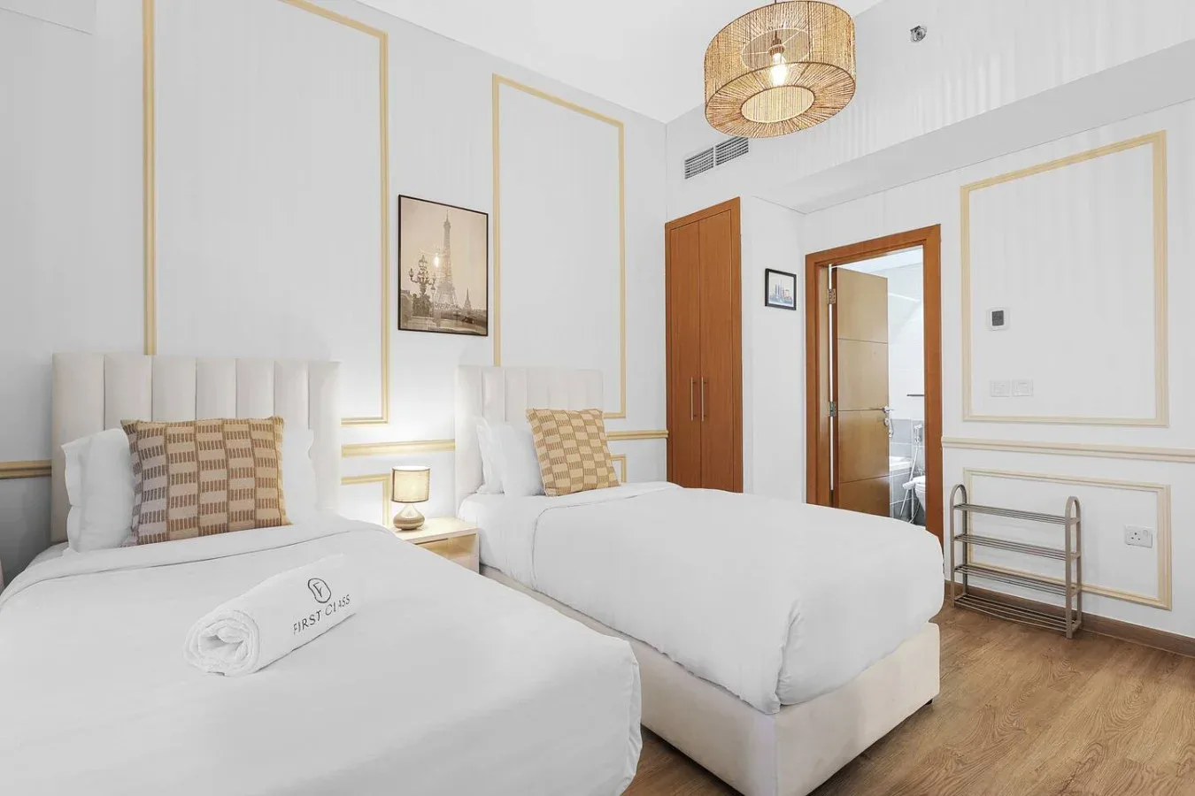 Un dormitorio luminoso con dos camas, ropa de cama blanca y paneles enmarcados.