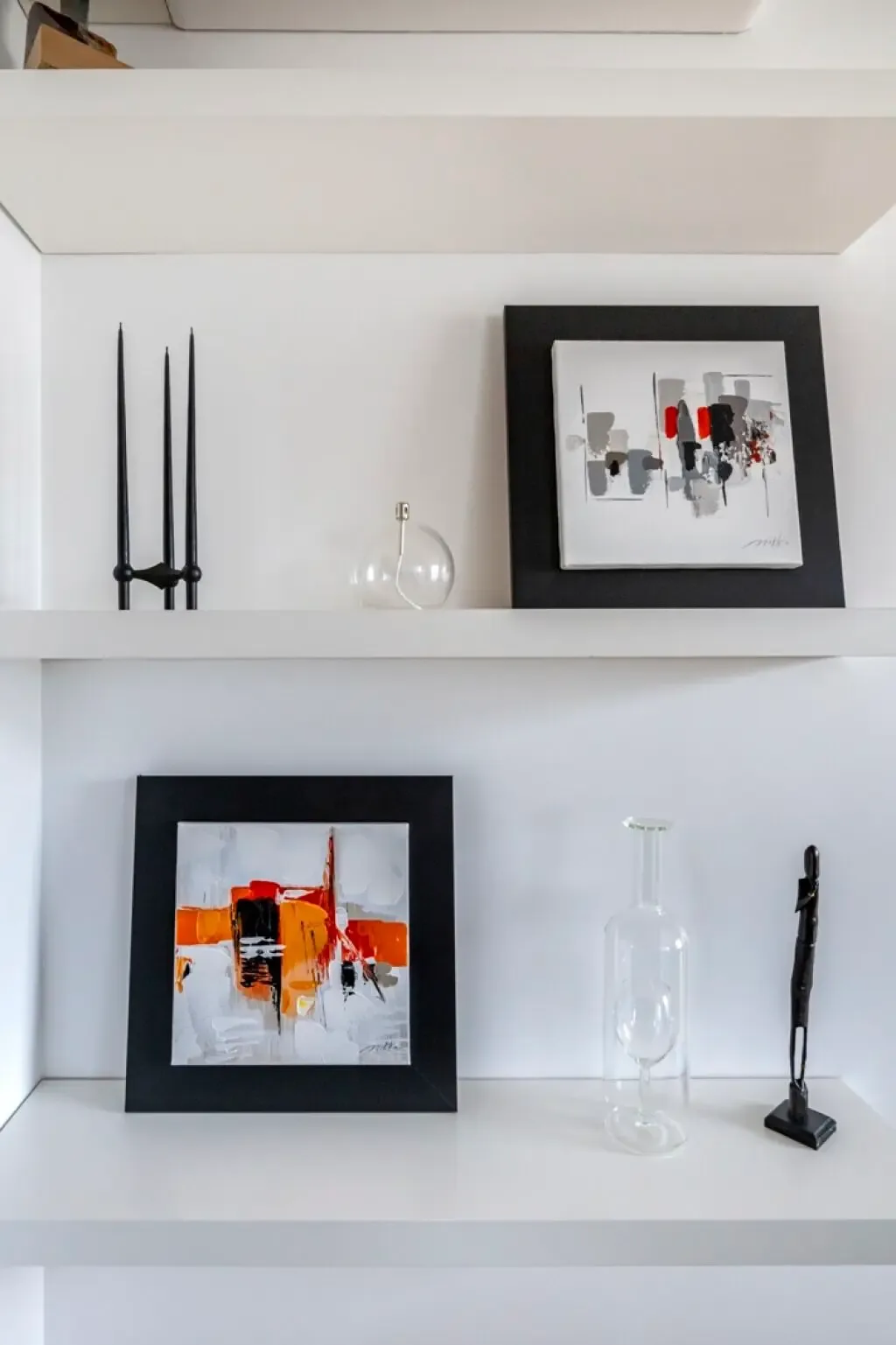 Abstract artwork and decorative objects are displayed on white shelves.
