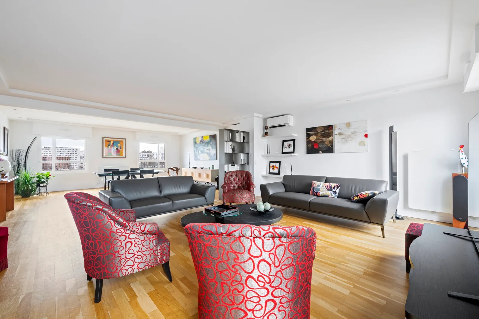 A bright living room with gray seating, red patterned chairs, and large windows.