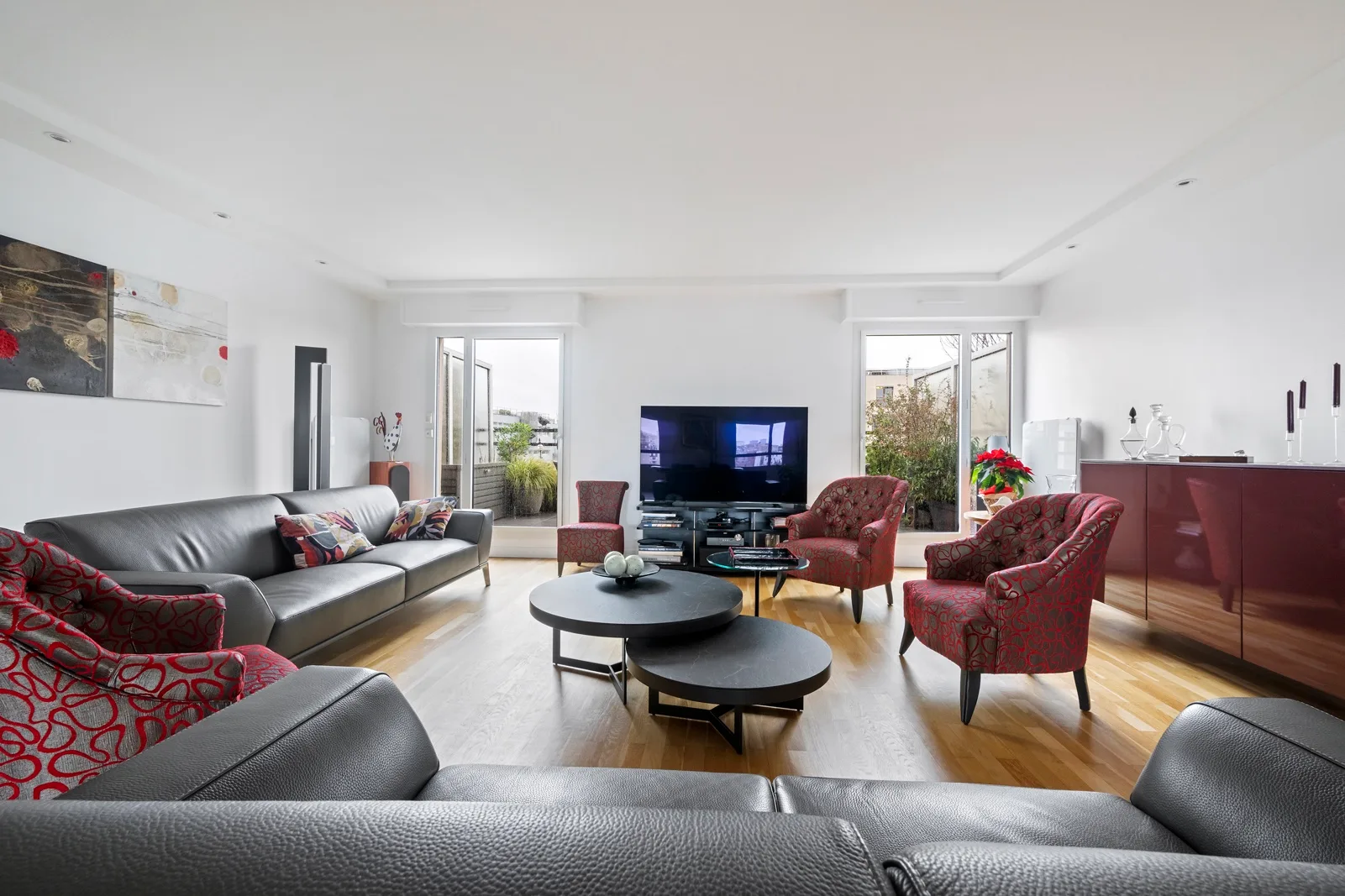A bright living room with dark seating, red armchairs, and a television.