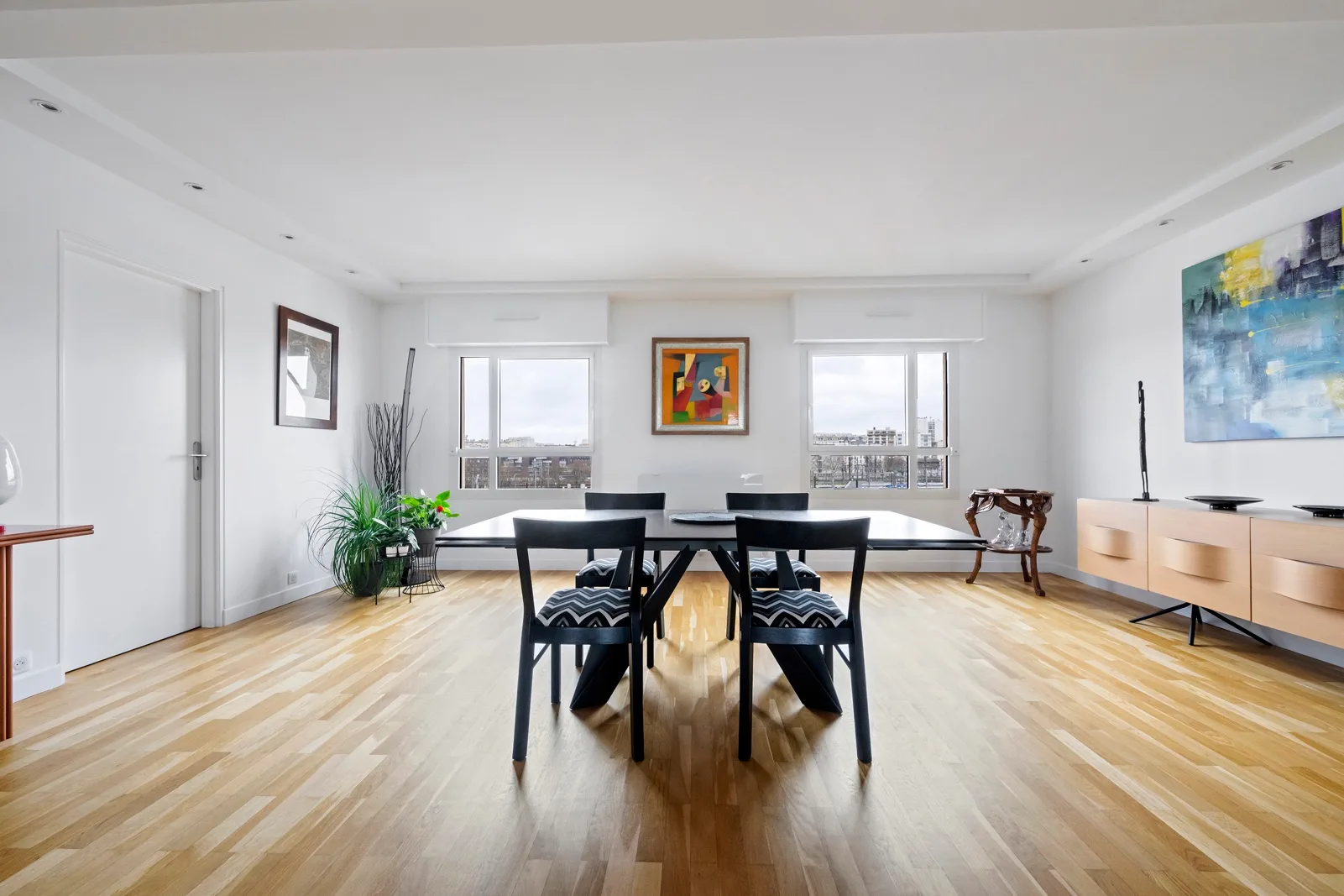 A bright dining area with a dark table and chairs beside large windows.