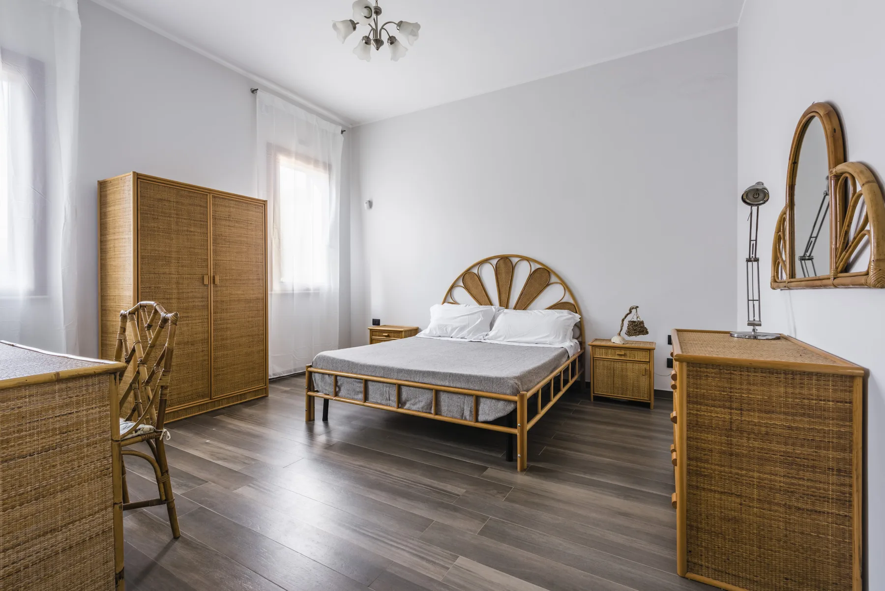 Un dormitorio luminoso con una cama, muebles de fibras trenzadas y ventanas altas.