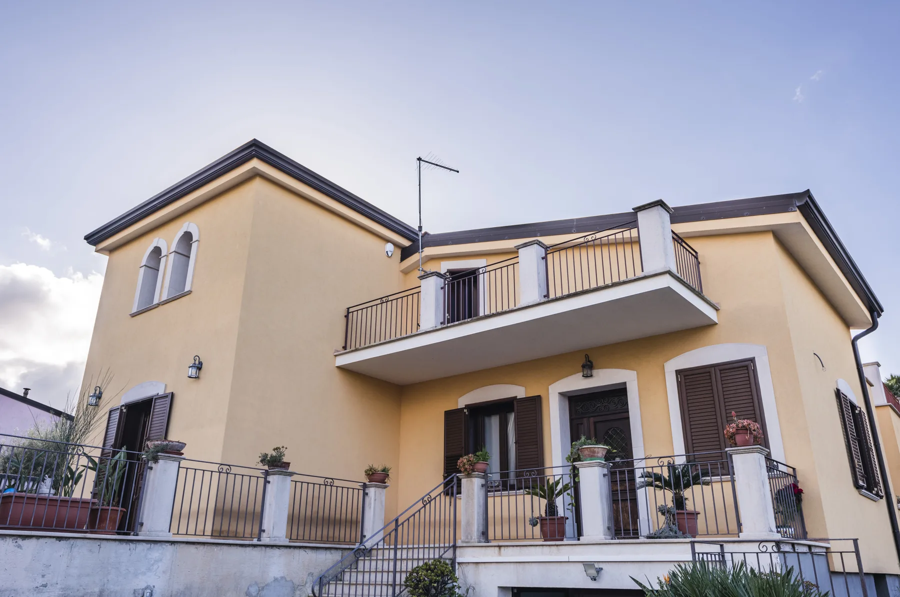 Una casa amarilla de dos plantas con balcones y macetas en las barandillas.