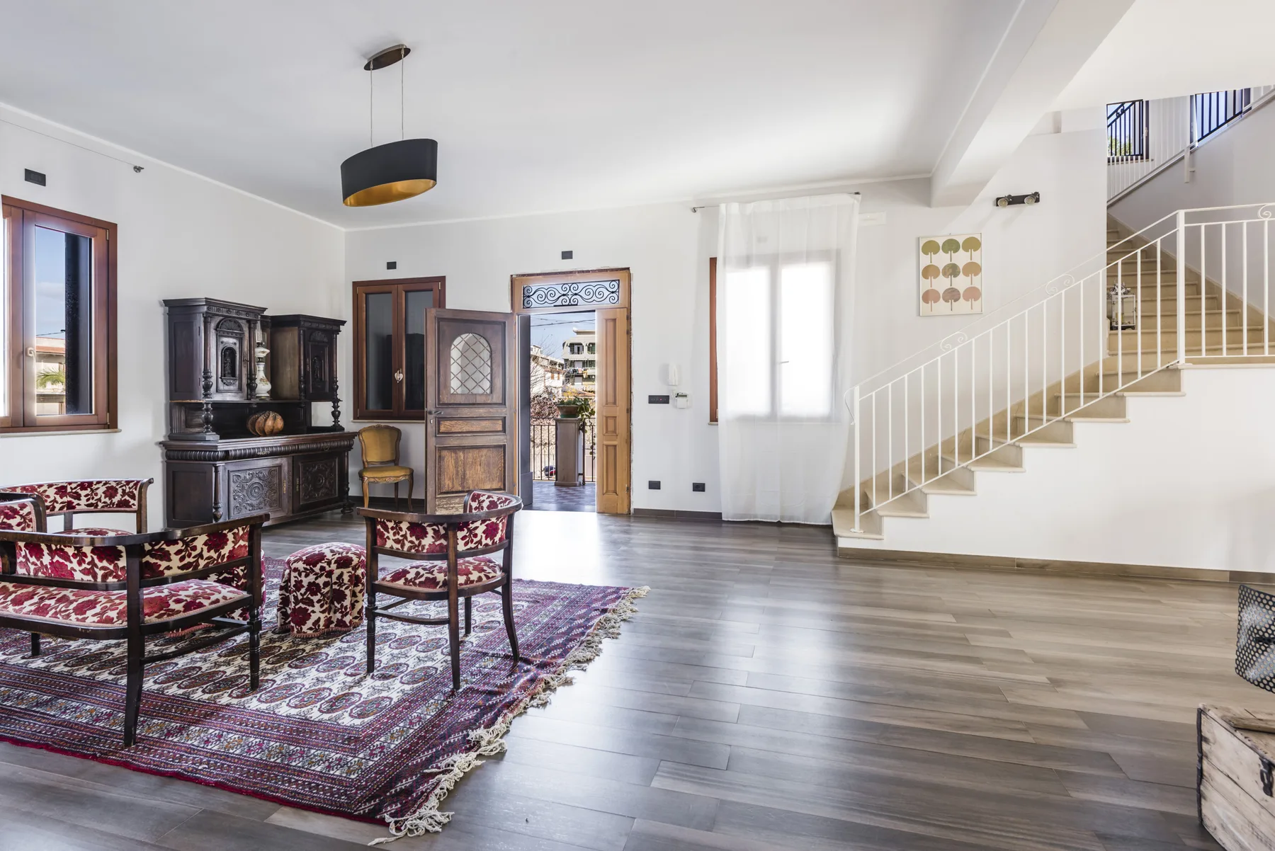 Una sala luminosa con asientos estampados, un mueble oscuro y una escalera.