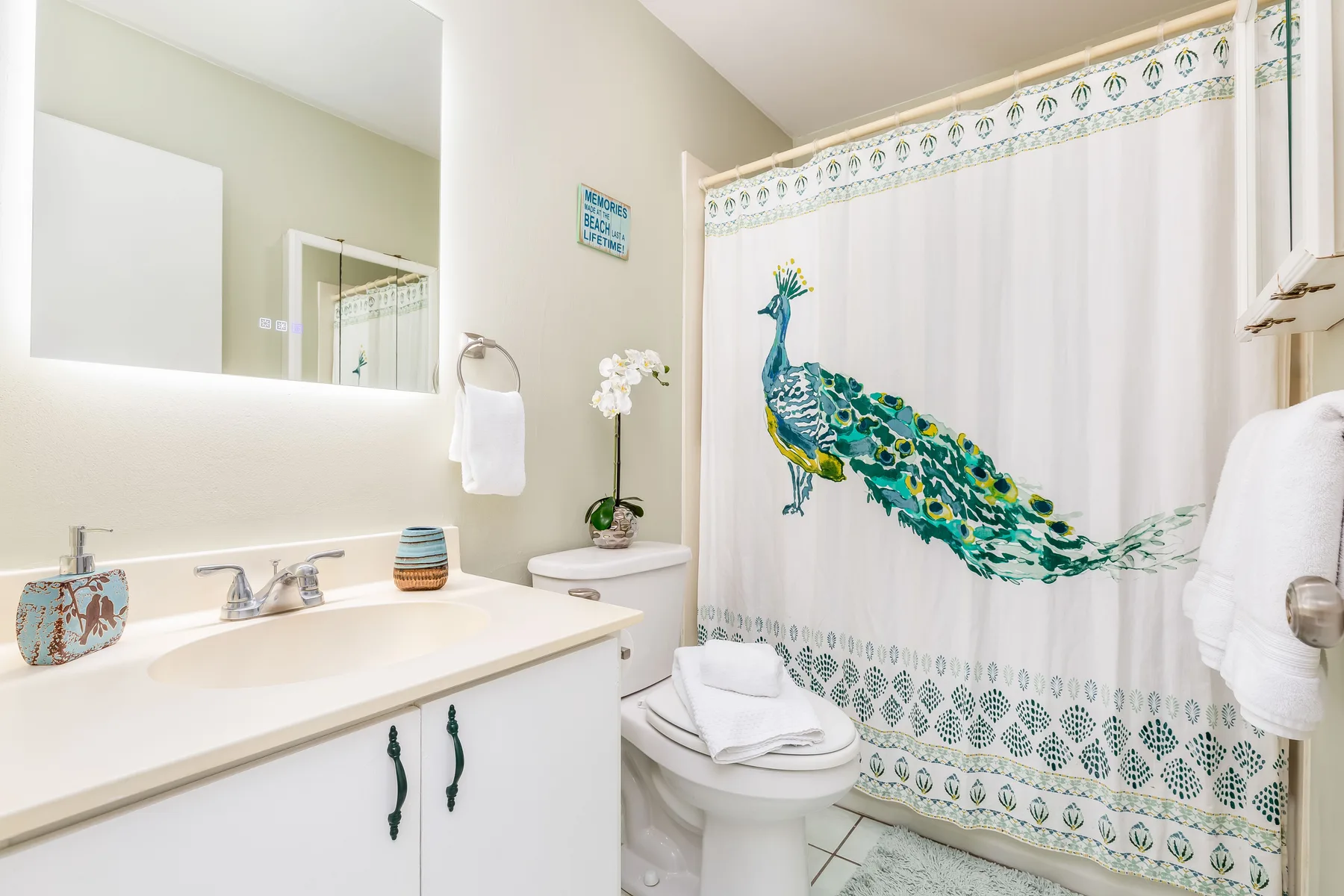 A bright bathroom features a sink, toilet, and a shower curtain with a peacock design.