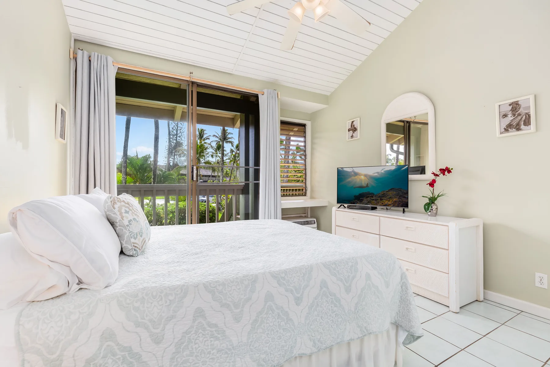A bright bedroom with a bed, dresser, and sliding glass doors opening to a balcony.
