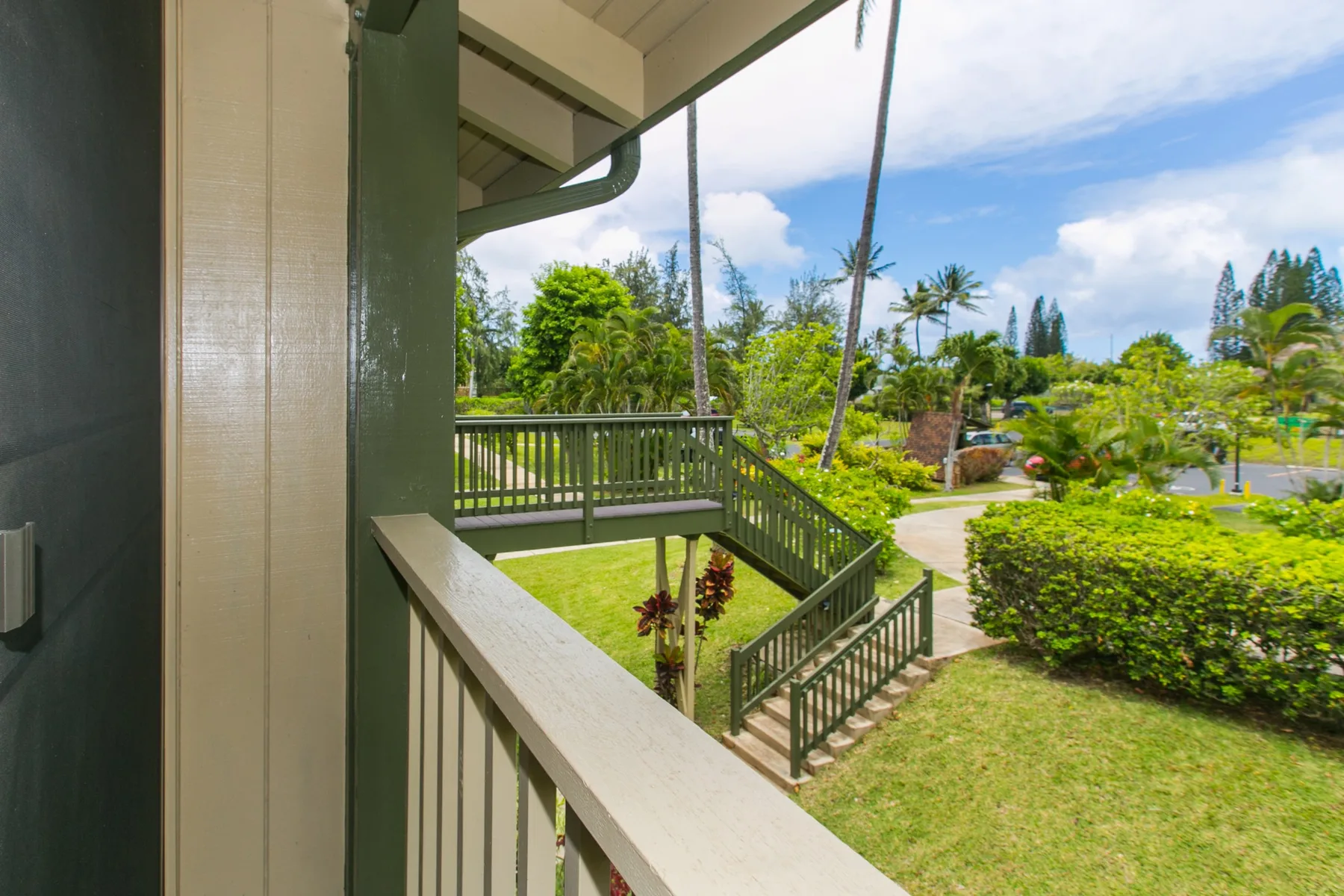 A covered porch overlooks a green garden with a path and tropical plants.