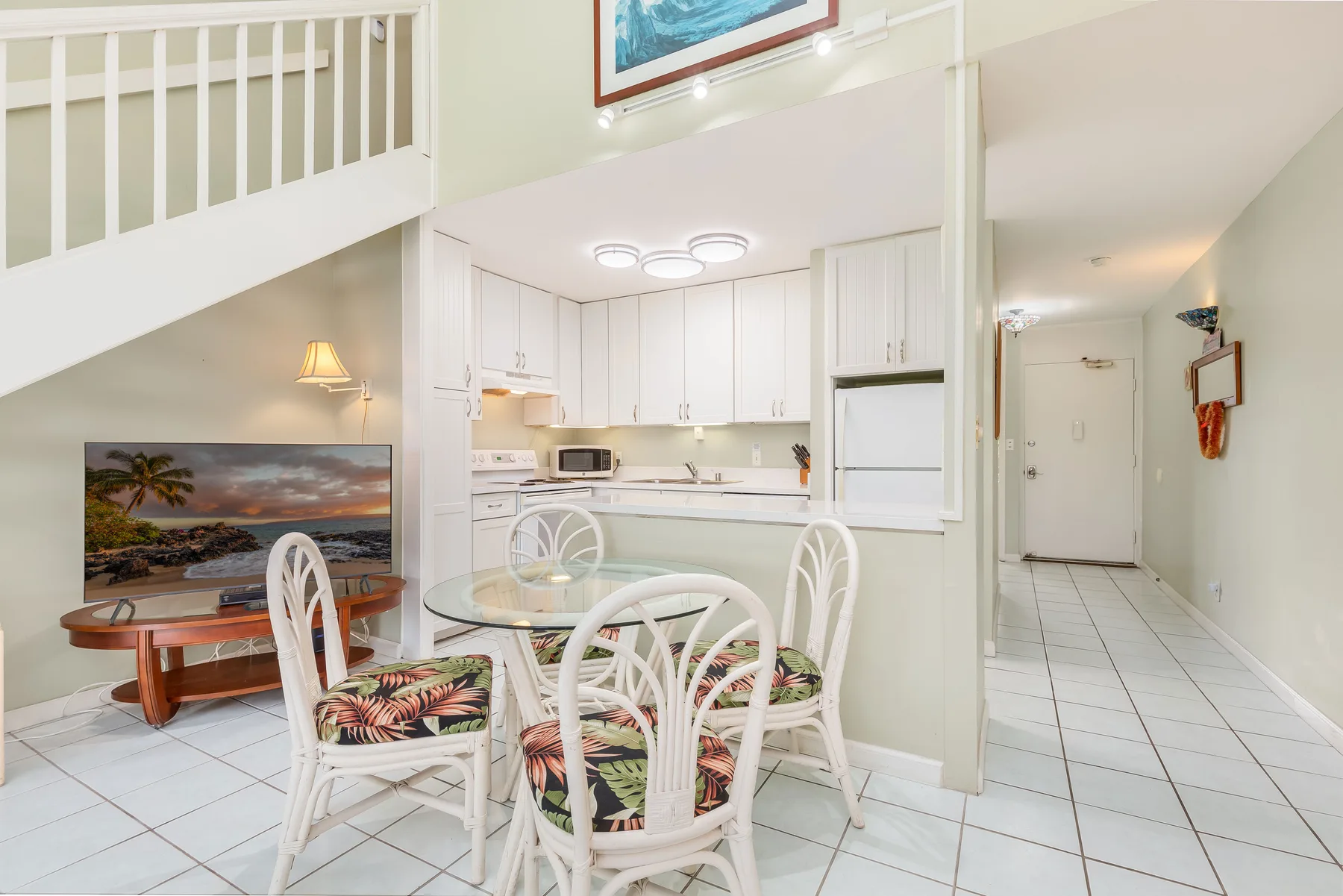 A bright dining area opens onto a white kitchen, with a staircase overhead.