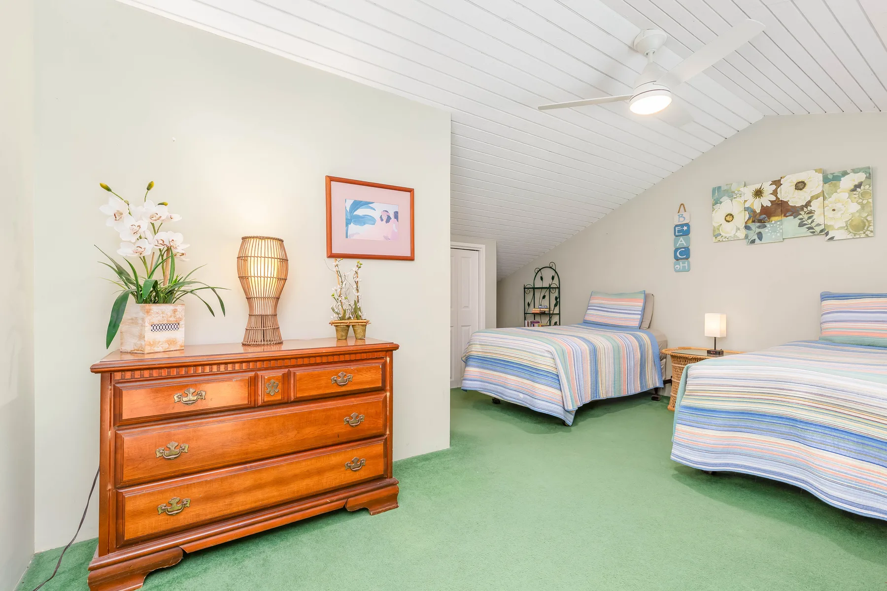A bedroom with two beds, a wooden dresser, and green carpet.