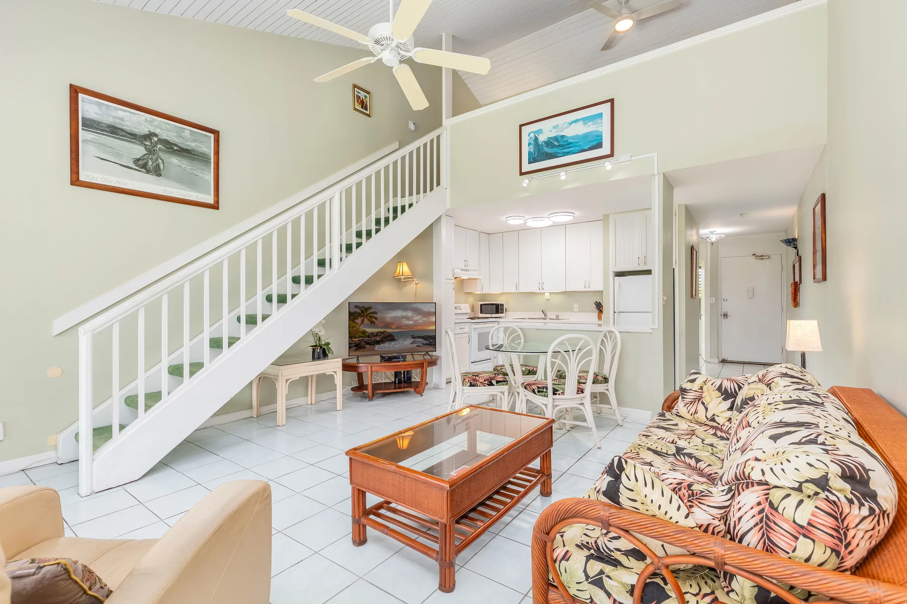 A bright living room with patterned seating, a coffee table, and a staircase beside the kitchen.